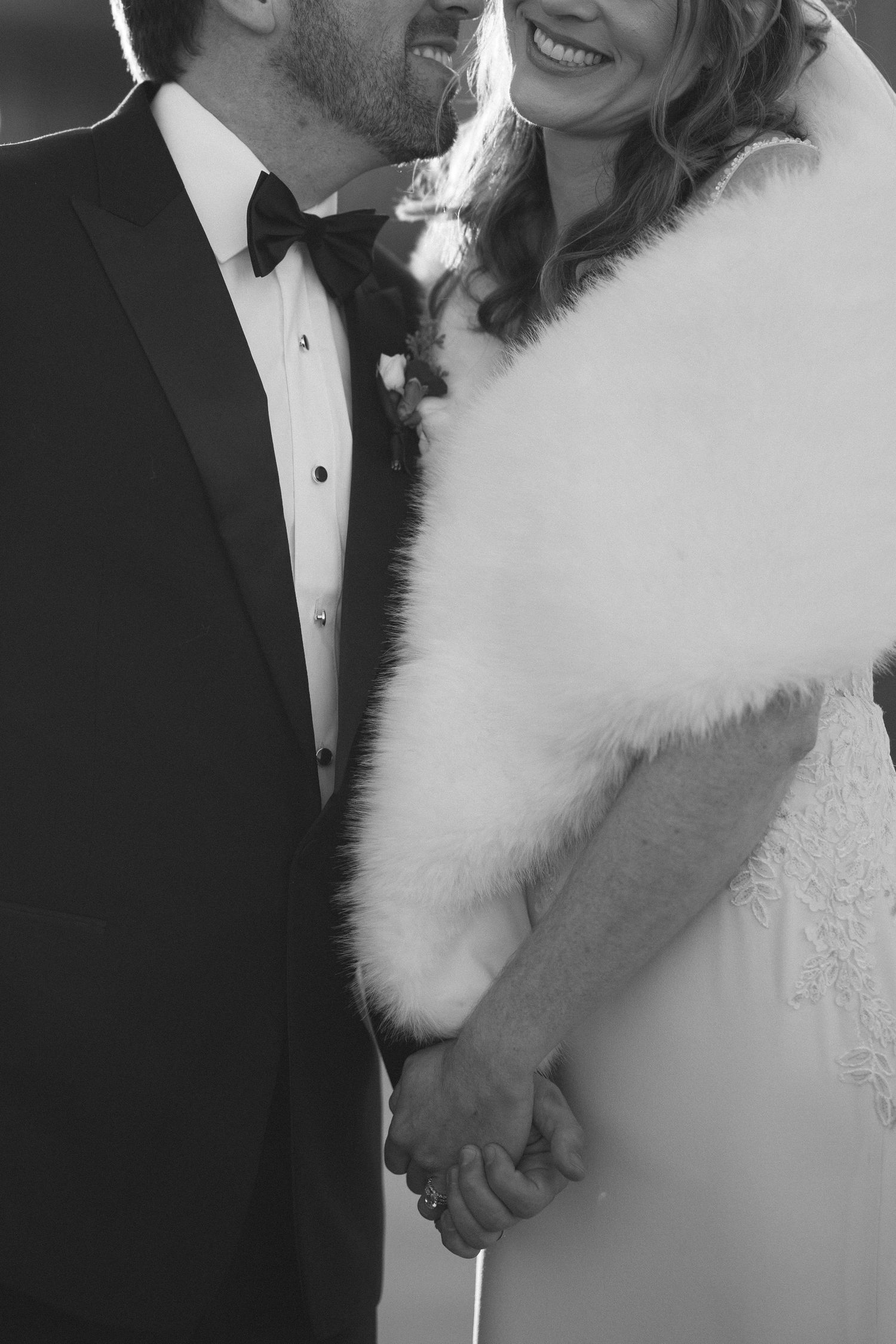 Black and white close-up of newlywed couple in formal wedding attire holding hands while wearing tuxedo and white dress.