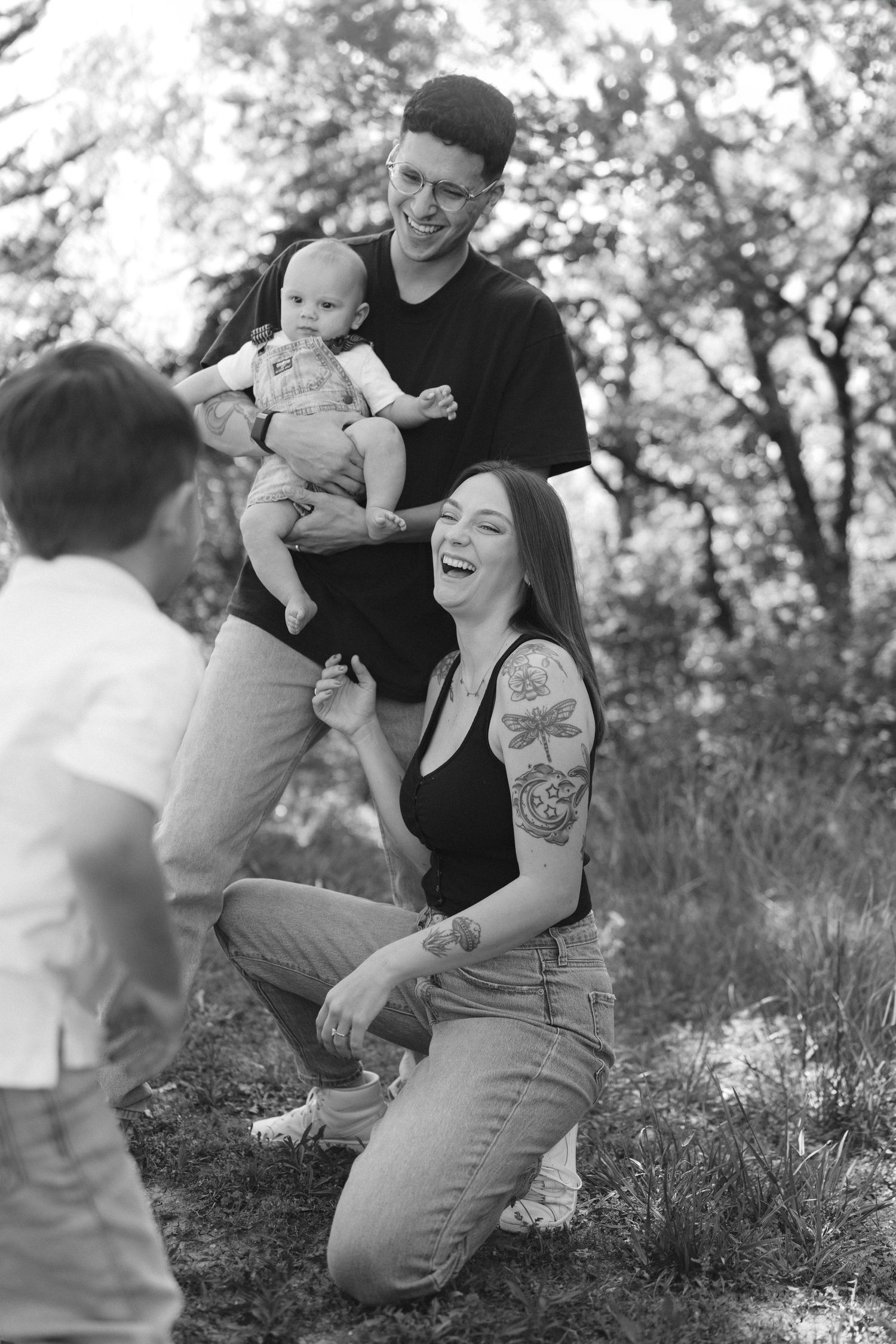 A candid black and white family photo outdoors showing joyful laughter and interaction in a natural setting.
