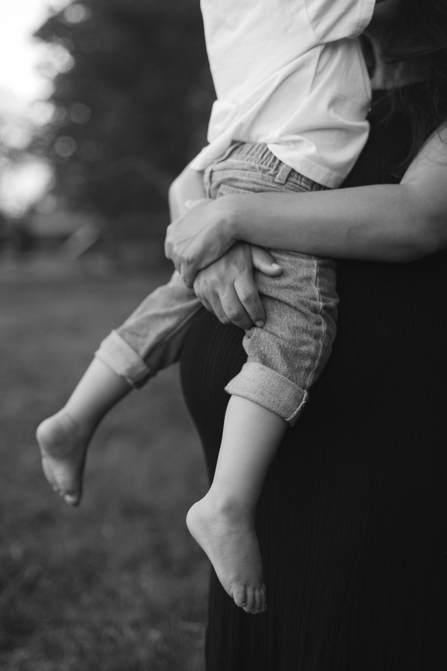 Close up black and white photo of small child's legs being held by adult hands. Wedding photographer Hannah Rogg Taylor