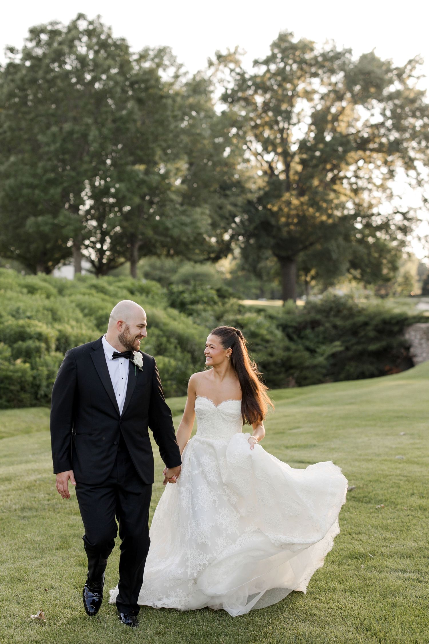A couple in wedding attire shares romantic moments together on a lush green hillside during golden hour.