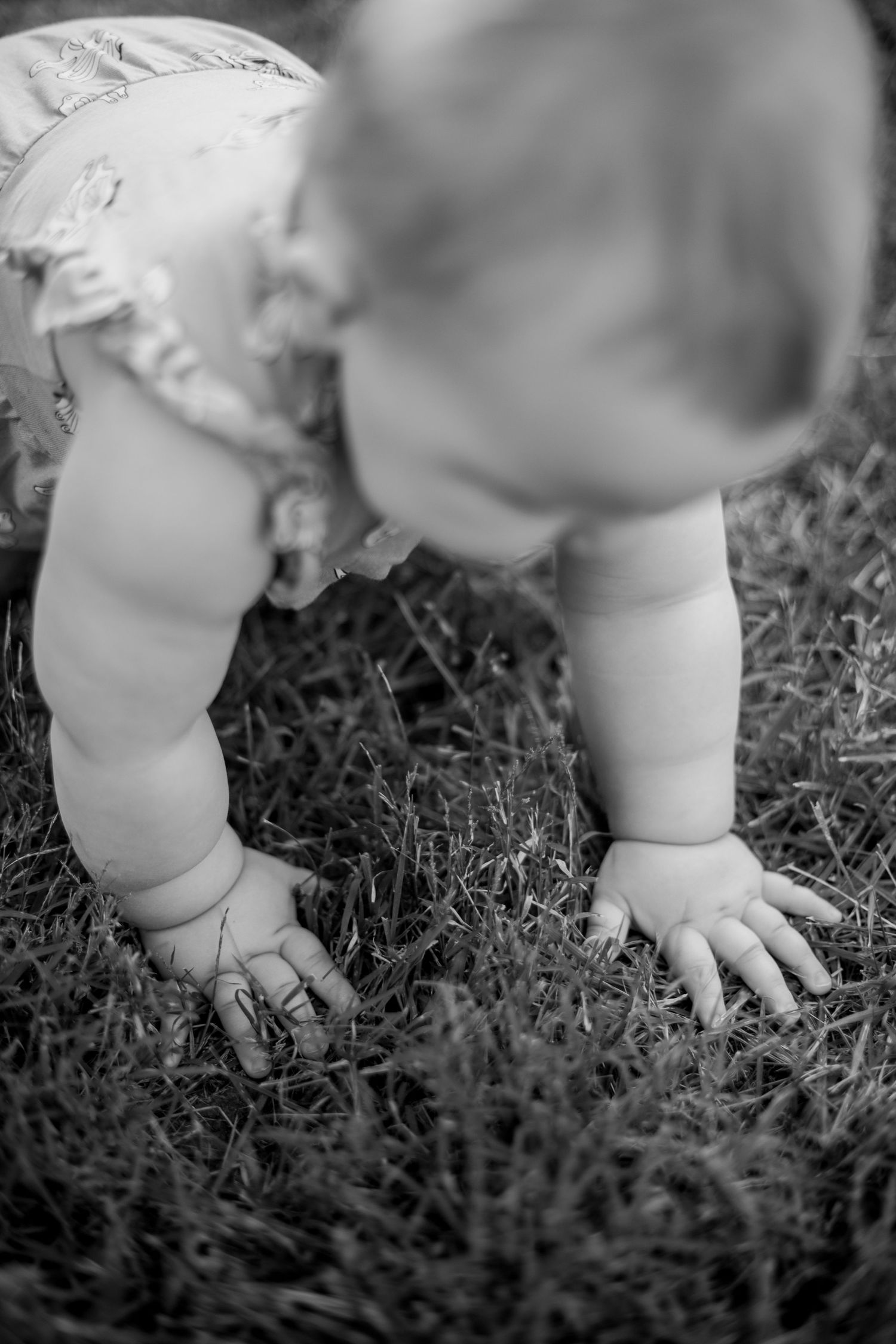 Black and white close-up of baby's legs and hands touching grass. Organic family portraits in Kansas City.