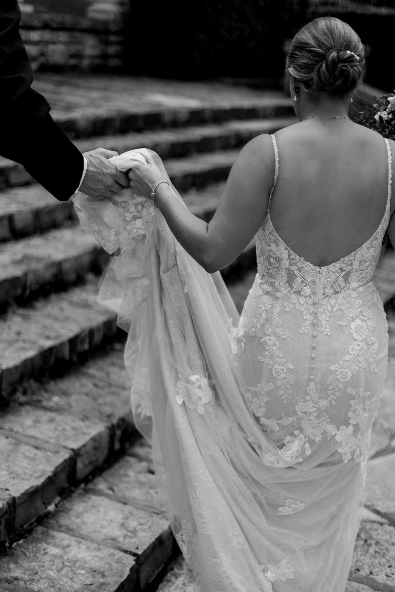 Detail of bride's lace wedding dress and hand holding train while ascending stone steps of the Verona Columns in Mission Hills Kansas.