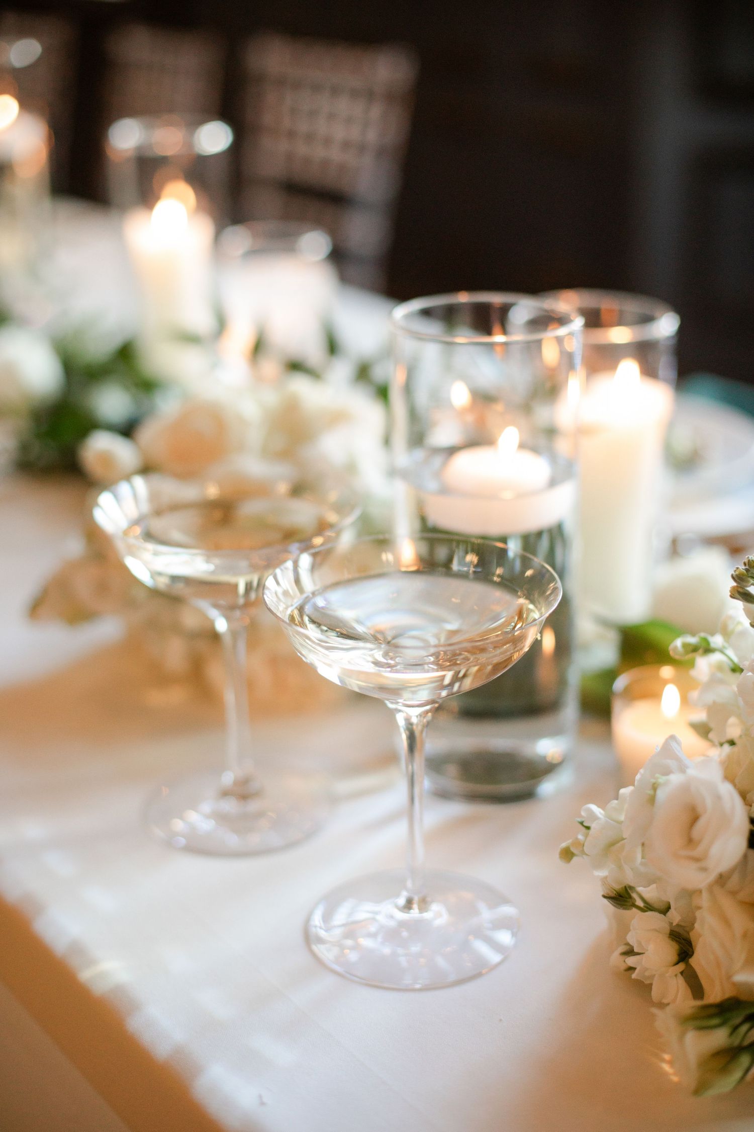 Elegant champagne glasses and white floral centerpieces line a wedding table with glowing candles creating romantic ambiance.