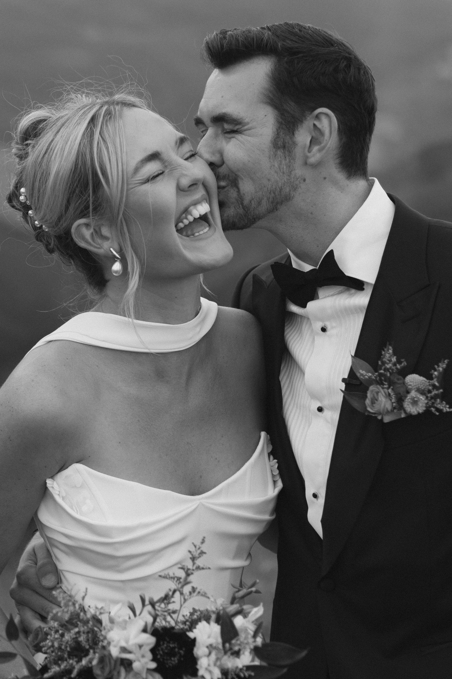 Black and white candid wedding photo capturing a joyful moment between newlyweds during an intimate outdoor celebration.