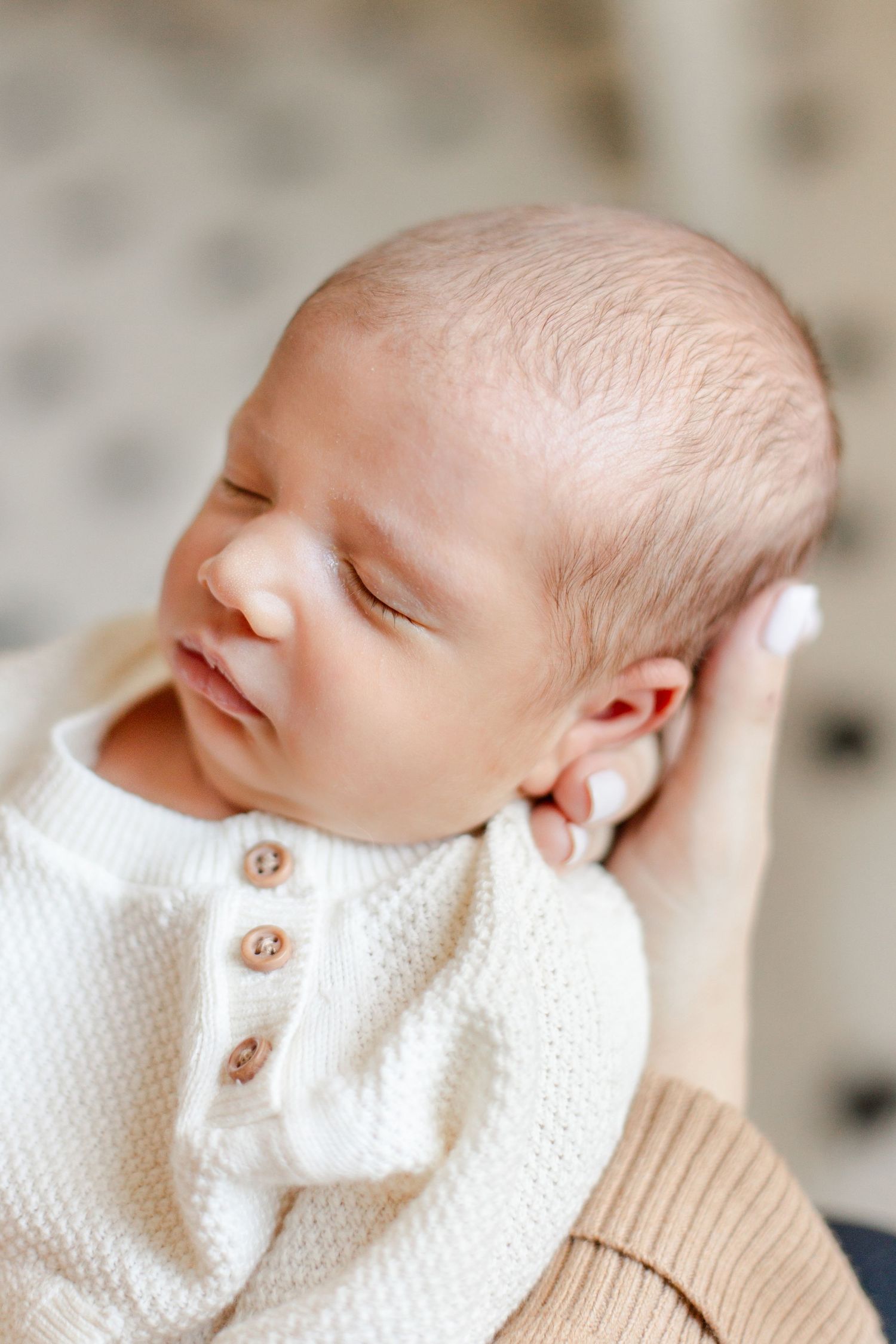 Peaceful sleeping newborn wearing white knit outfit against neutral background.