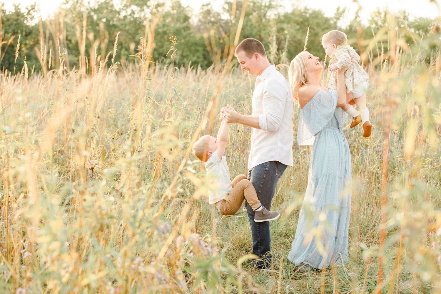 Family enjoying a playful moment together in a sunlit meadow.