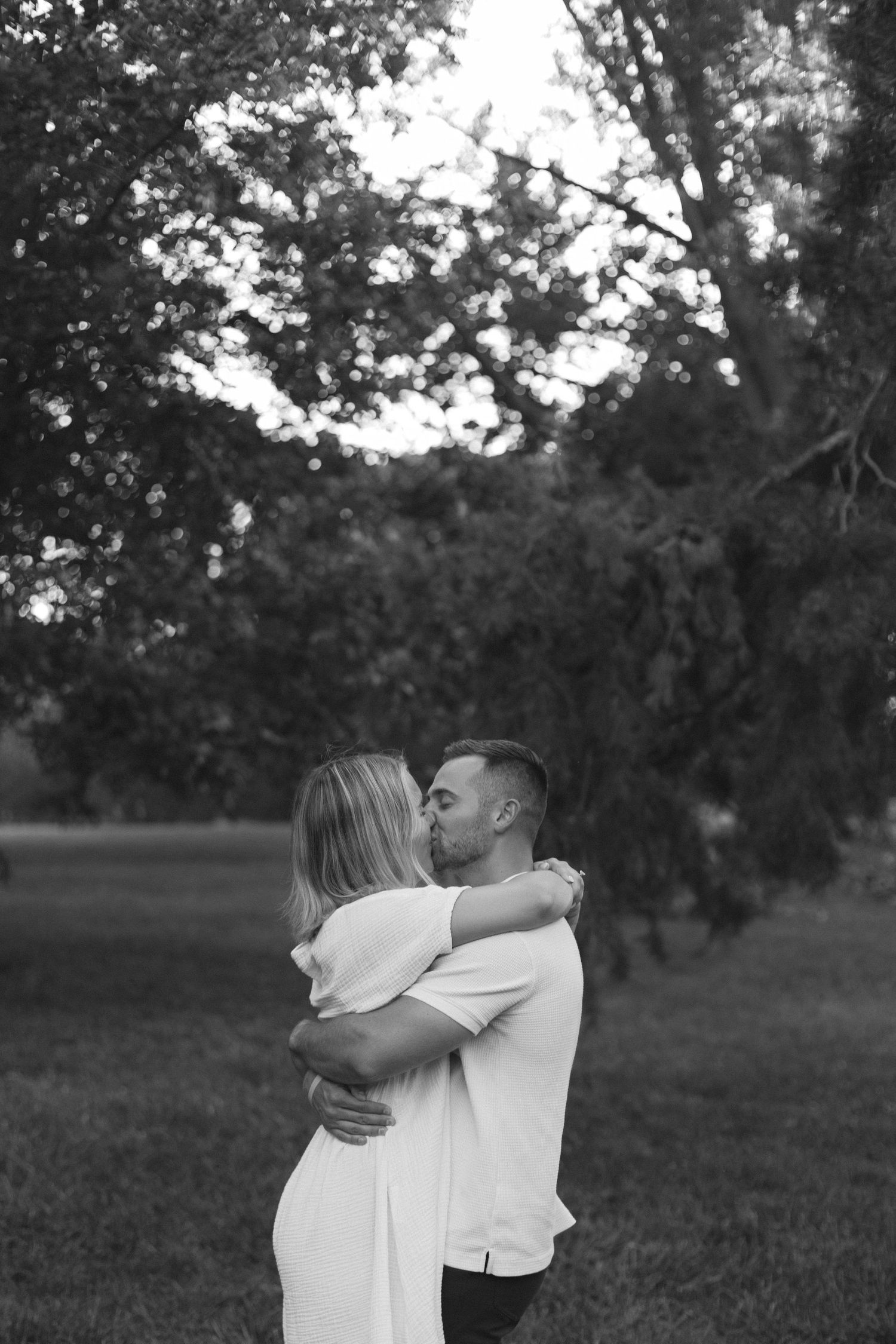 Intimate black and white photo of couple embracing under tree canopy. Authentic candid engagement photos in Kansas City.