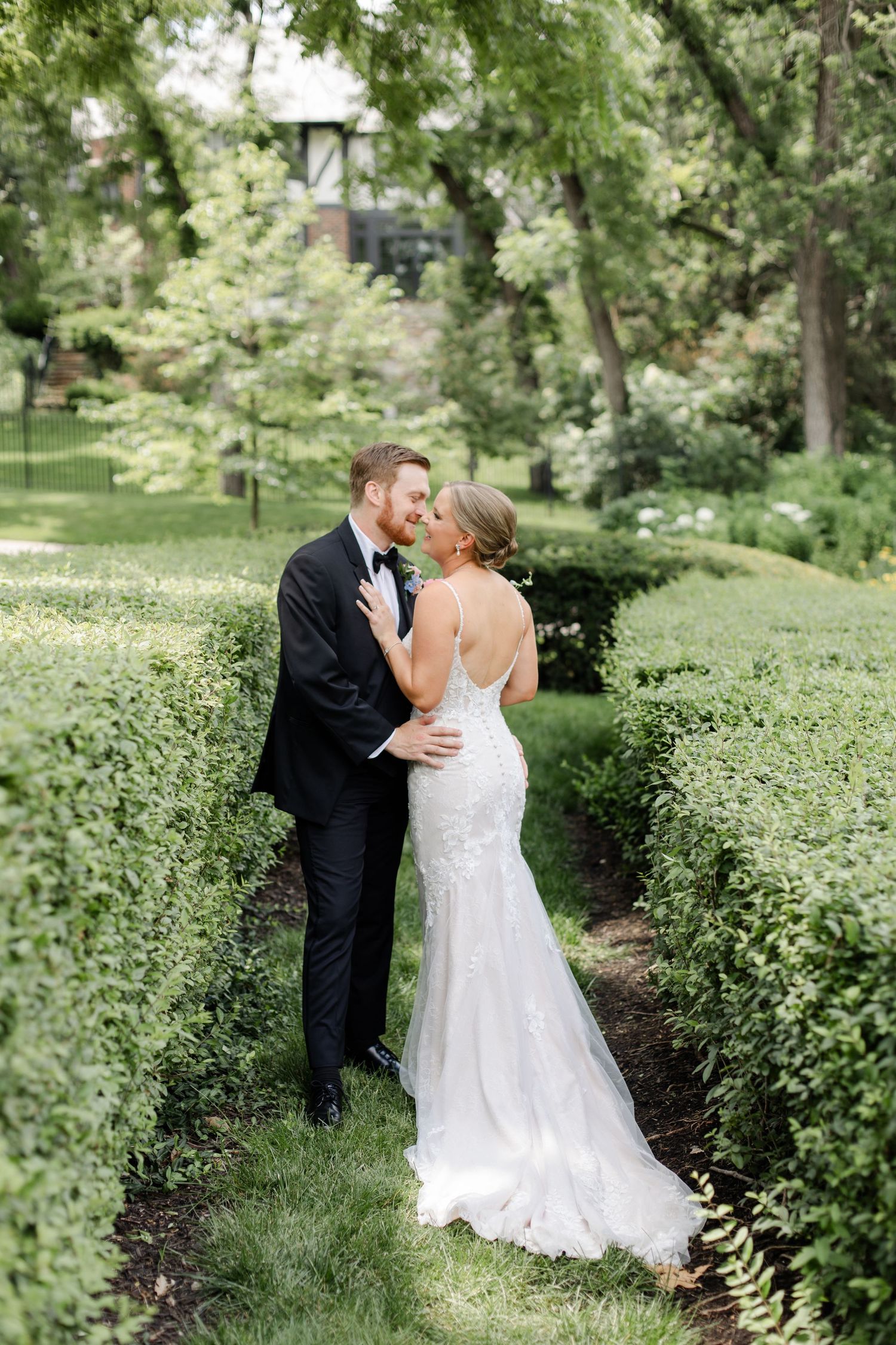 Romantic wedding couple embraces on a garden path surrounded by lush greenery.