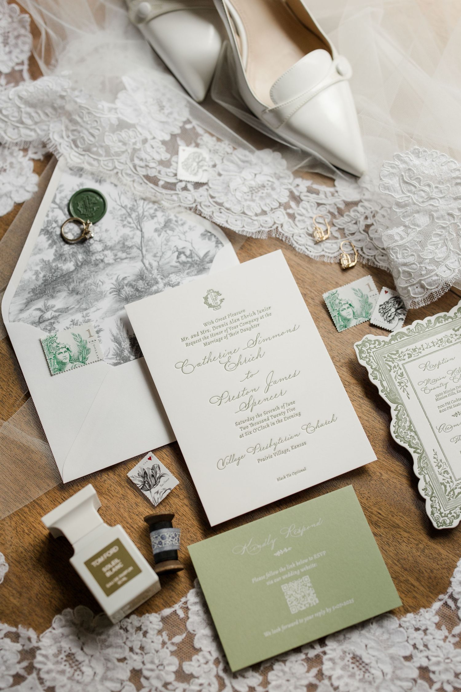 Elegant wedding invitation suite featuring white letterpress printing and sage green accents laid out on a wooden surface.