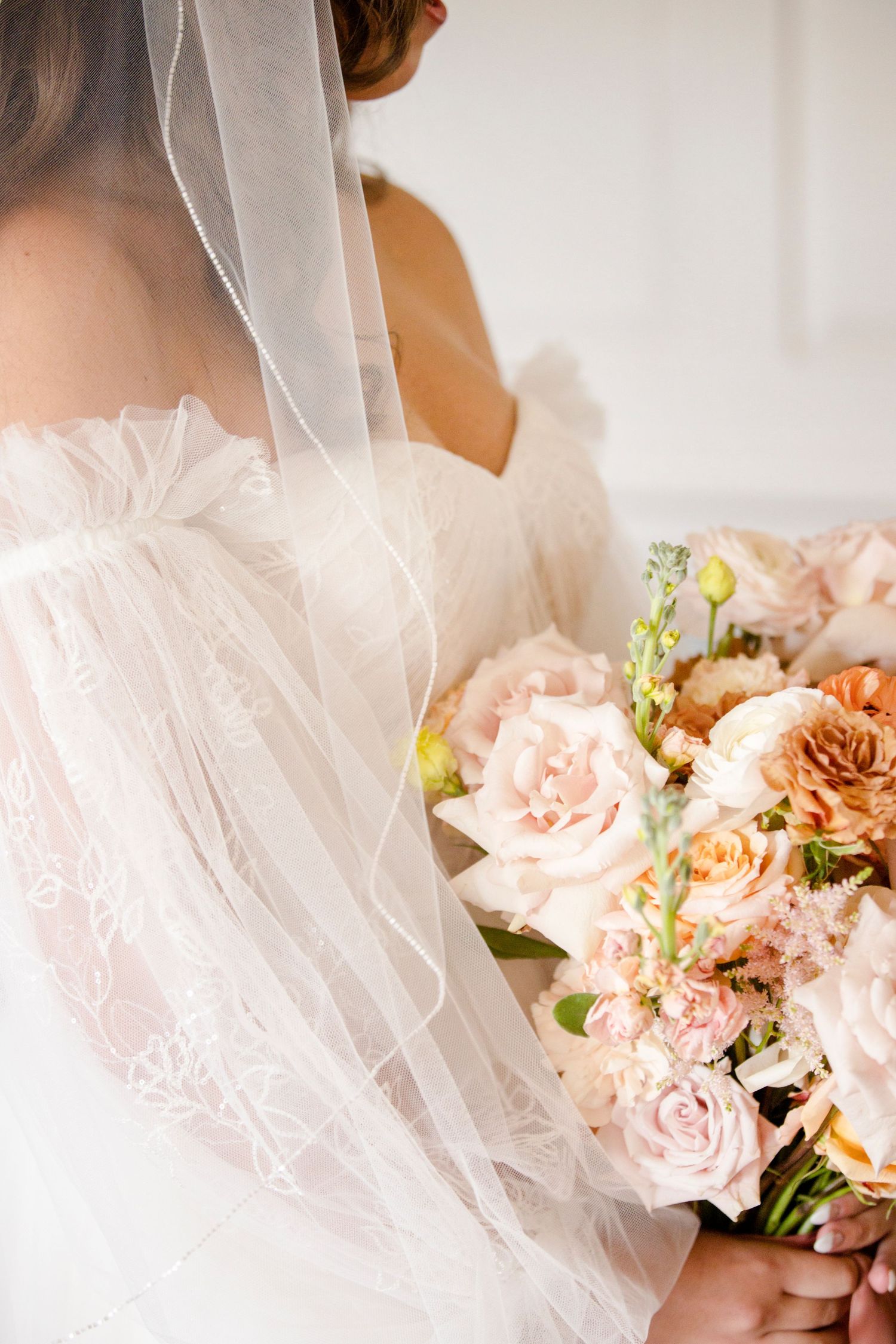 Delicate bridal veil and soft peach rose bouquet against white background.