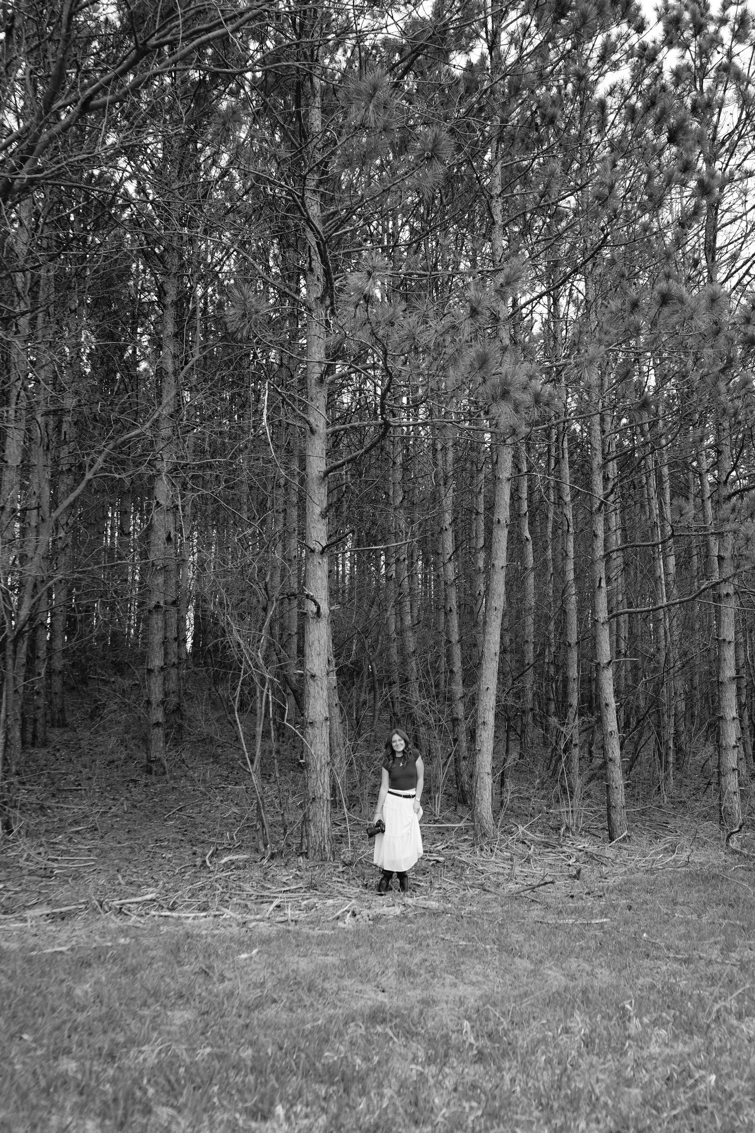 Black and white film photo of elizabethrophoto, wide shot standing by timber.