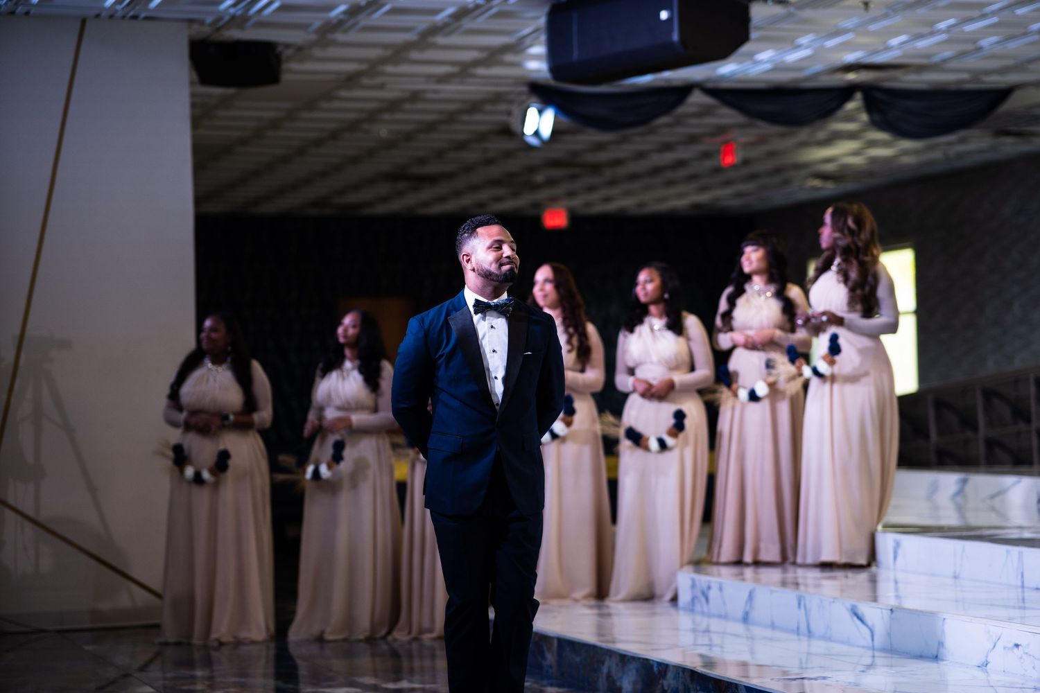 Groomsman walks in front of bridesmaids standing on stairs with floral bouquets.