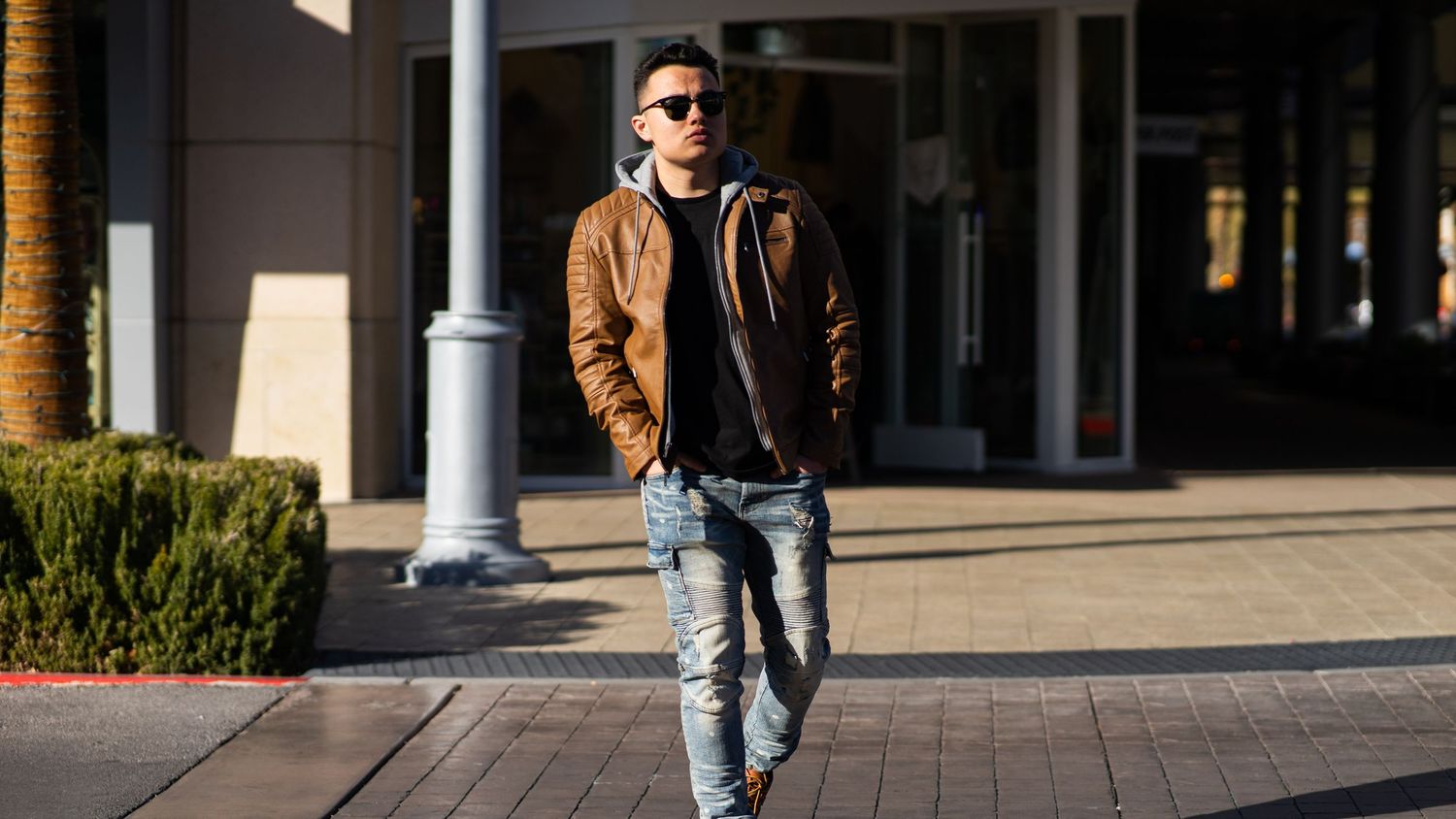 Man in leather jacket and sunglasses crossing the street.
