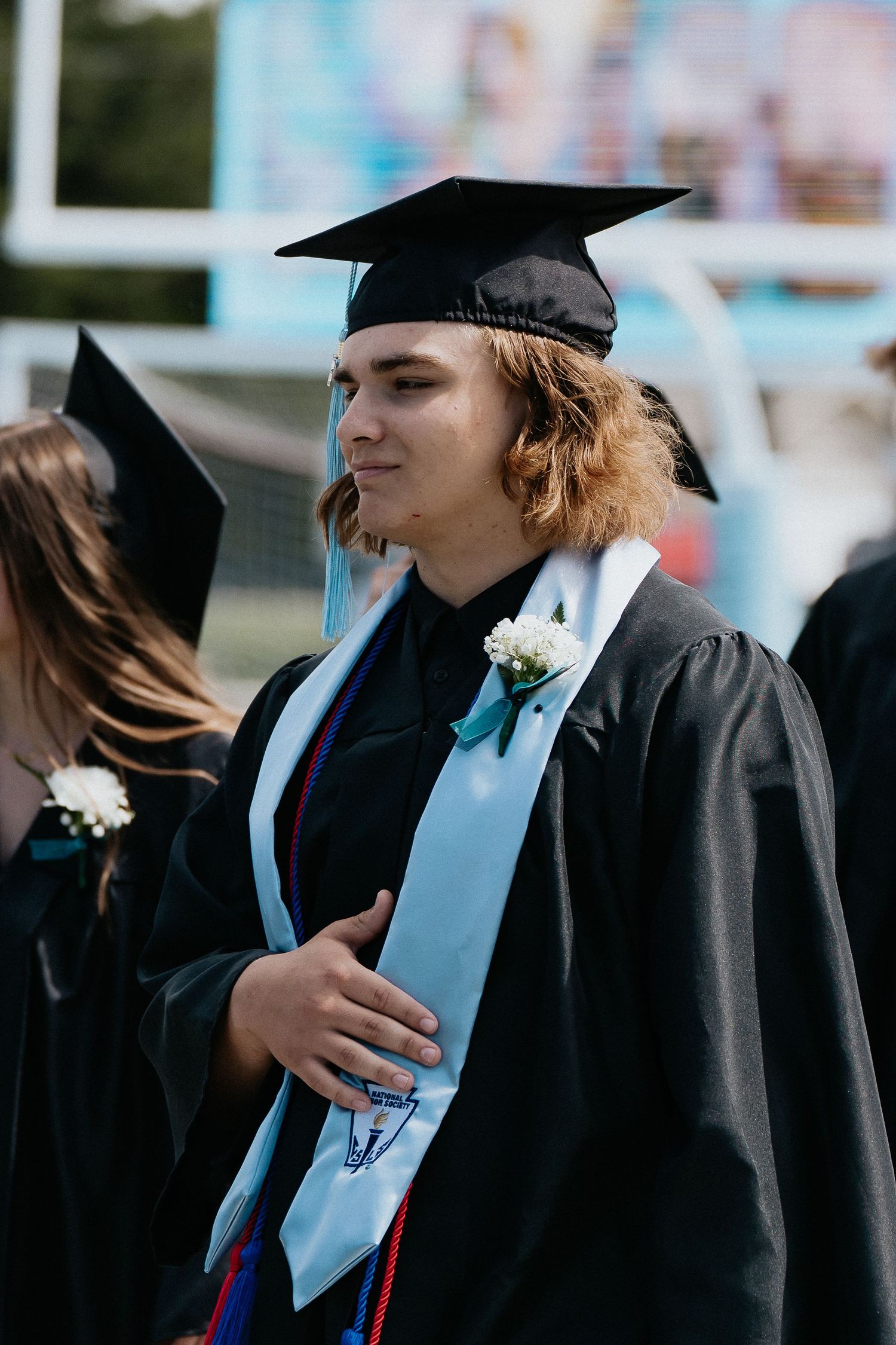 Graduates in black caps and gowns with light blue stoles standing in procession line.