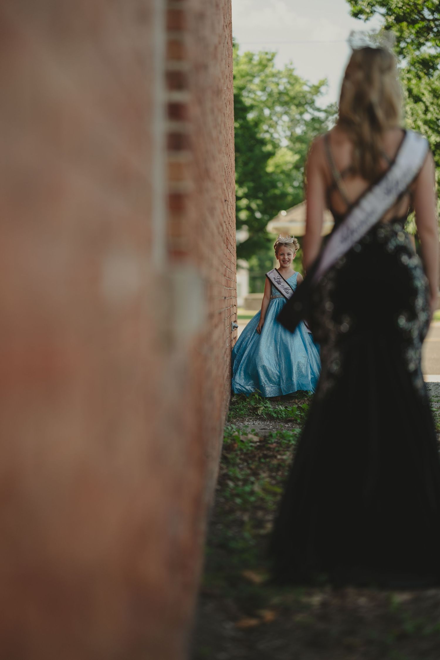 Artistic silhouette of two figures in formal wear against a brick wall with soft bokeh.