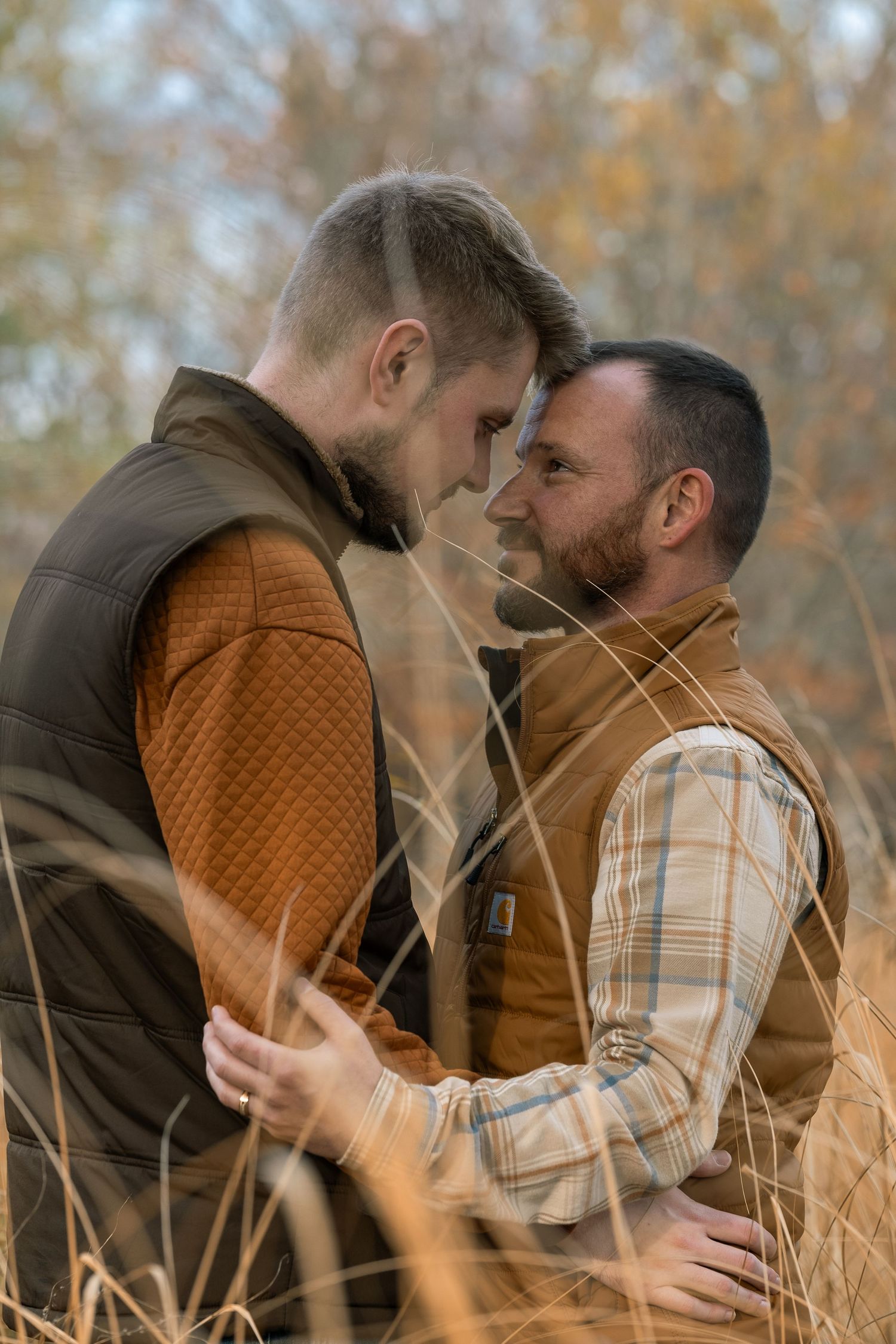 Intimate moment between couple in autumn field wearing warm layers.