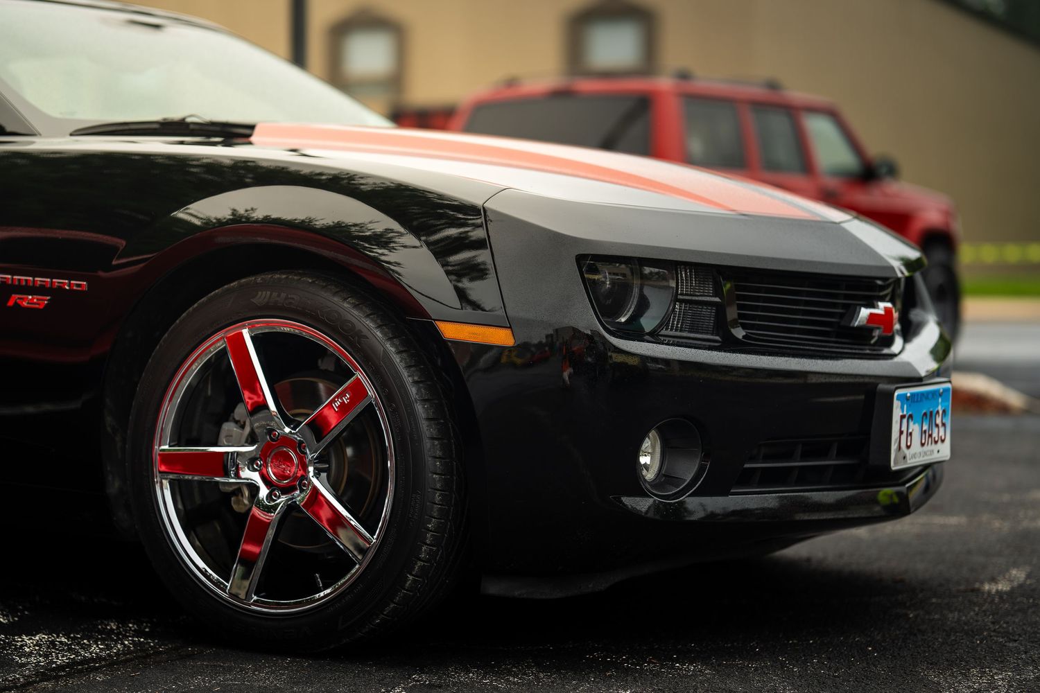 Low angle view of classic cars with custom wheels parked on wet pavement.