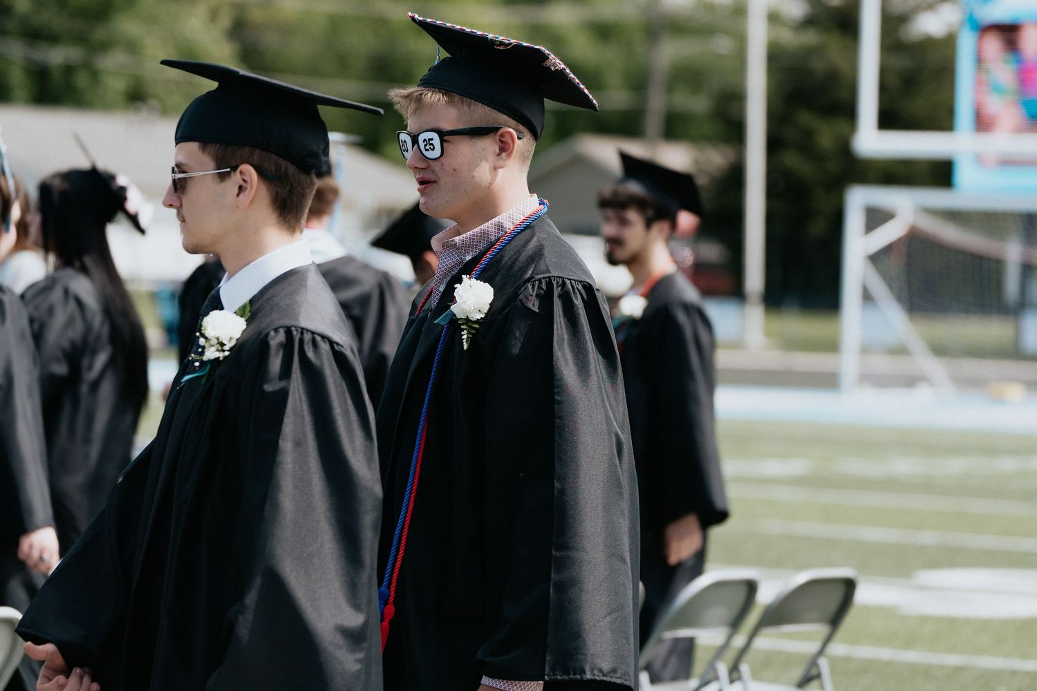 Graduates in traditional black academic regalia walking during outdoor commencement ceremony.