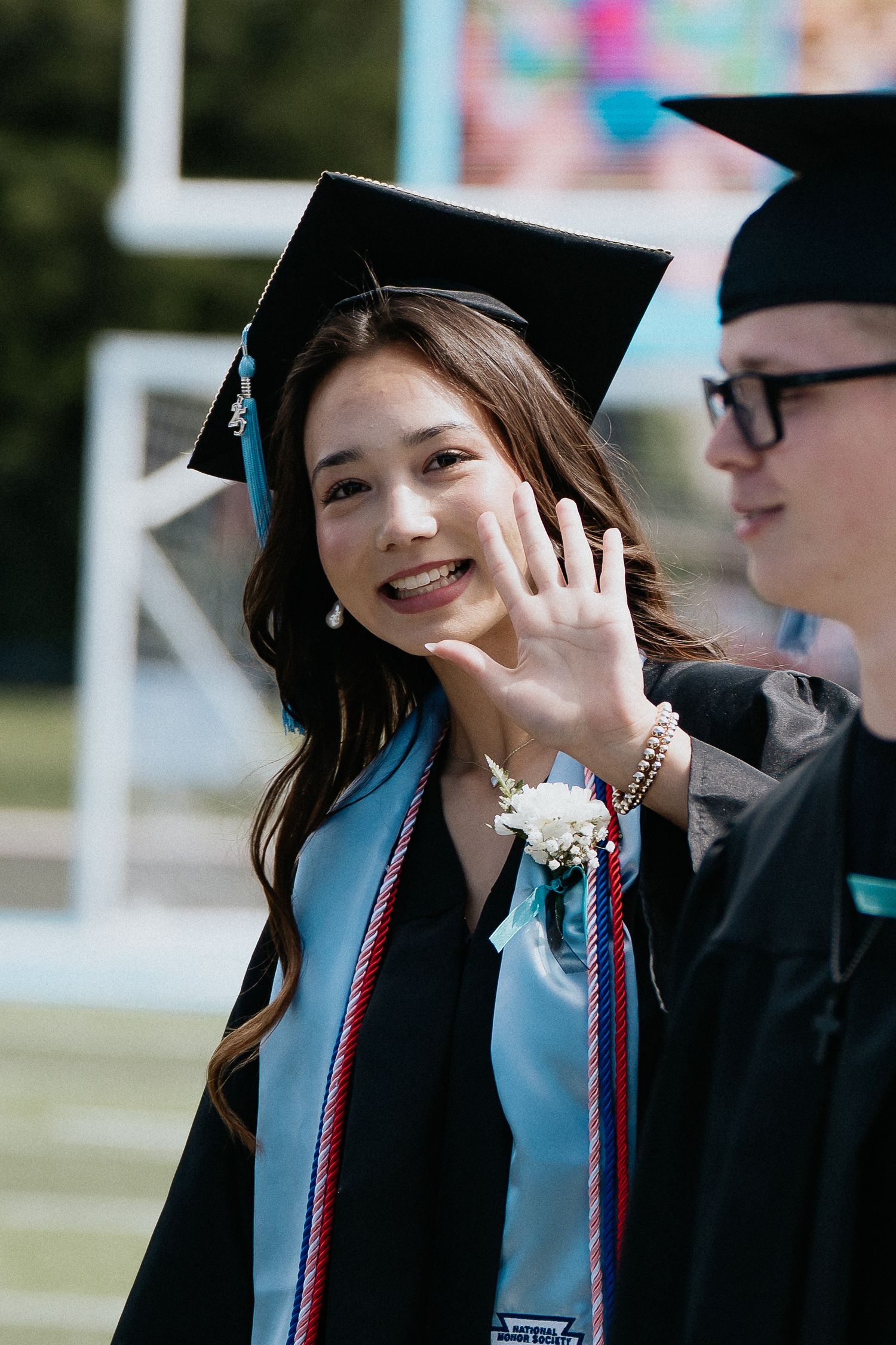 Graduate wearing a cap and gown with colorful cords during graduation ceremony celebrations.