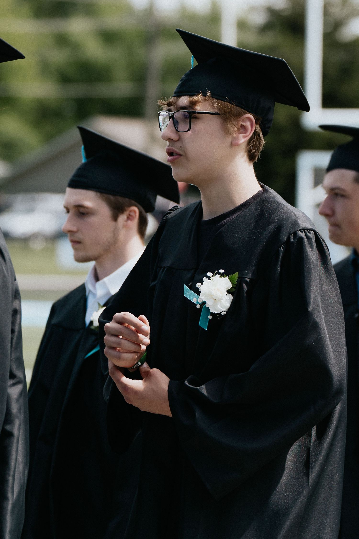 Row of graduates in black caps and gowns with light blue stoles during ceremony.