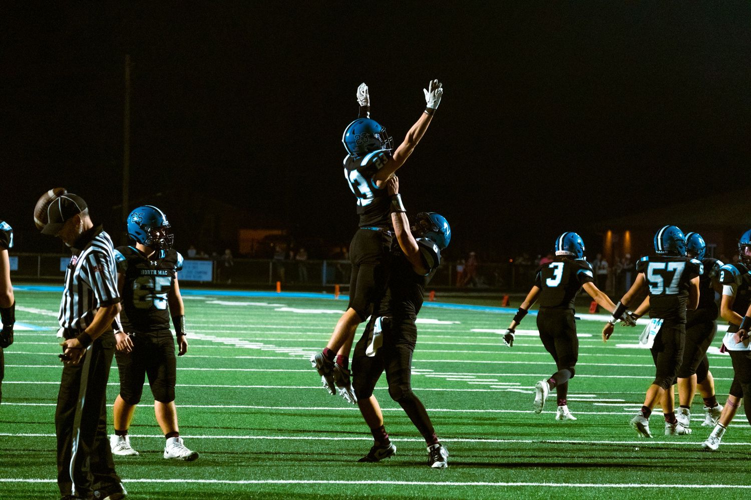 Athletes practicing football drills on a green turf field during nighttime training.