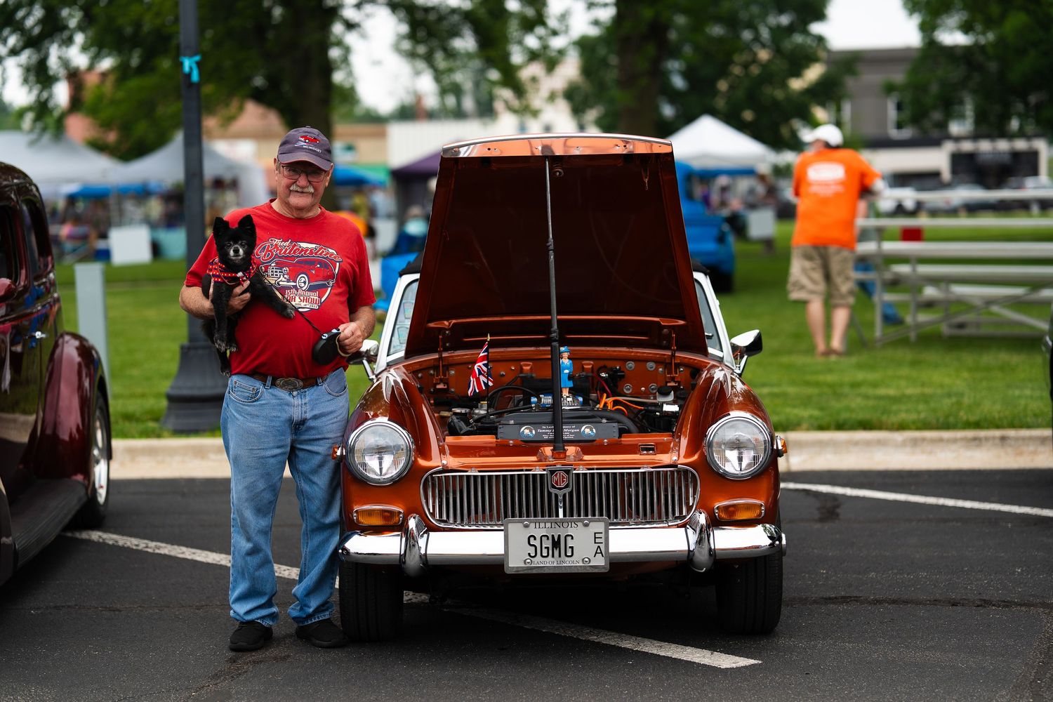 Vintage orange and chrome automobiles on display at an outdoor car show.
