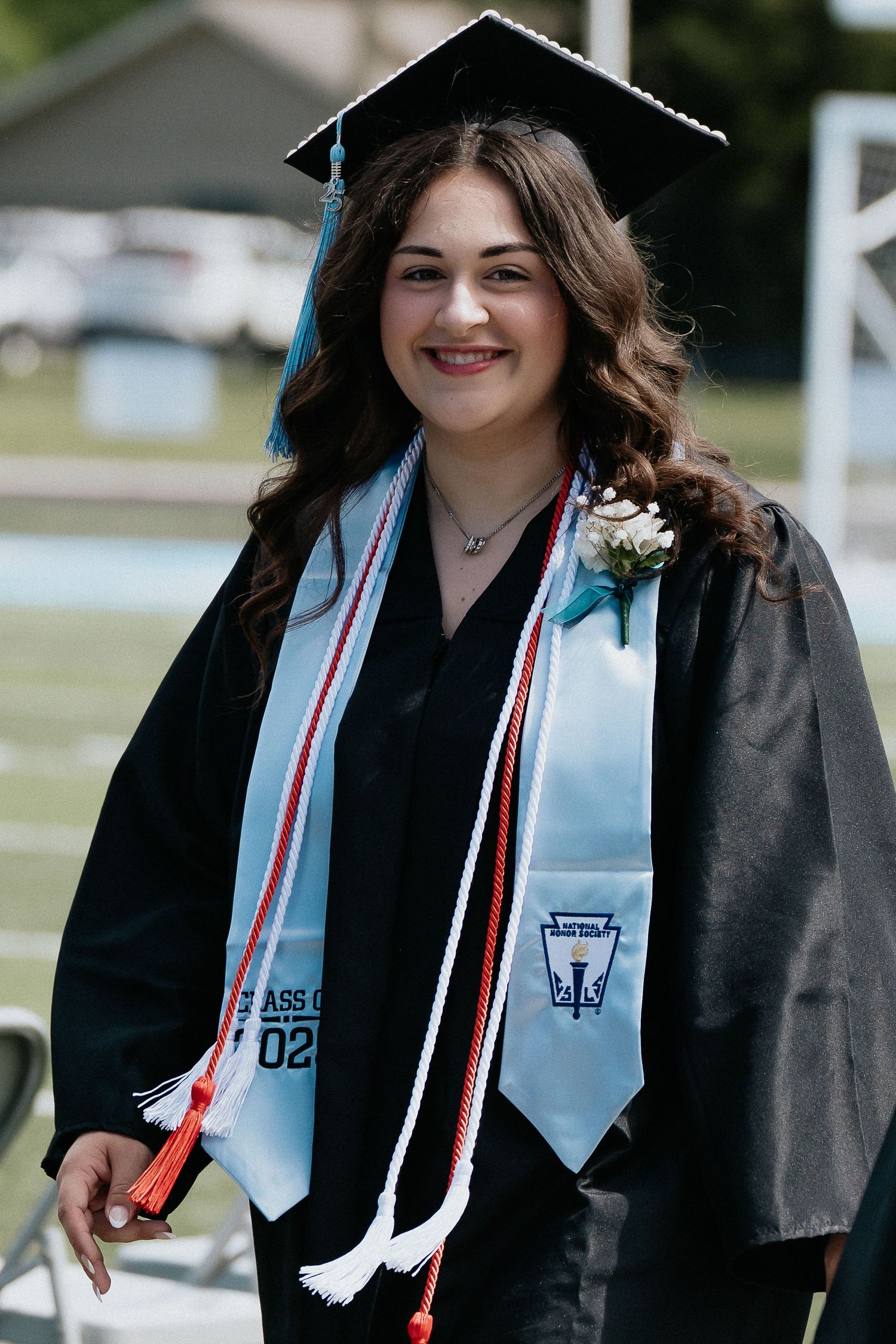 Graduate in cap and gown with light blue stole smiling during commencement ceremony.