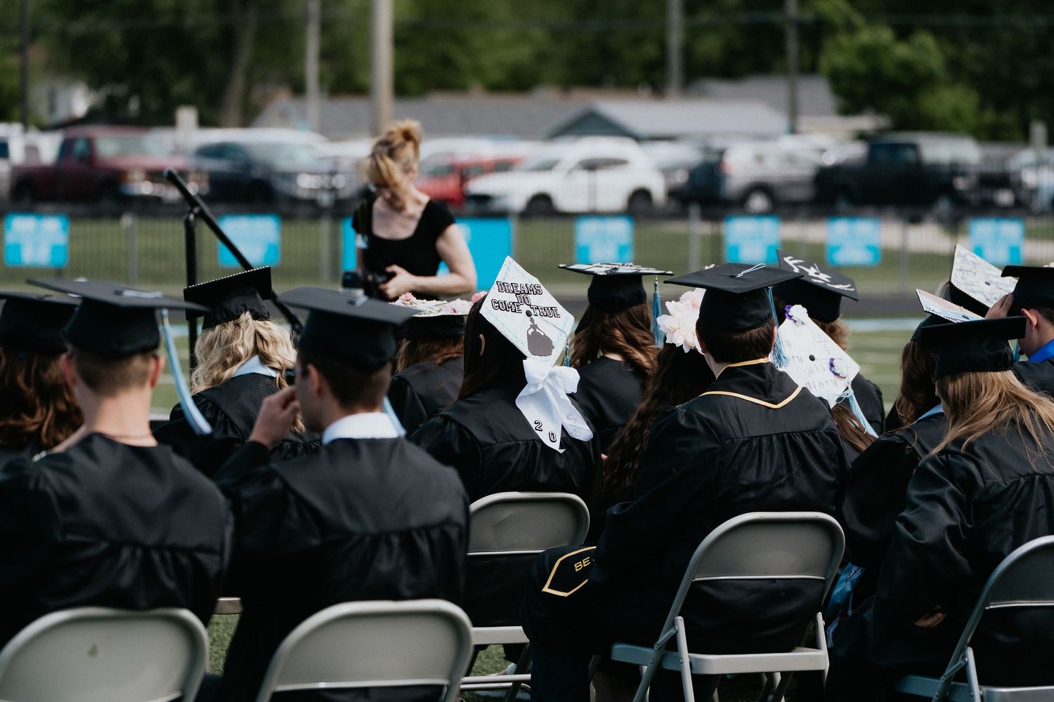 Graduates seated in rows of chairs during an outdoor commencement ceremony.