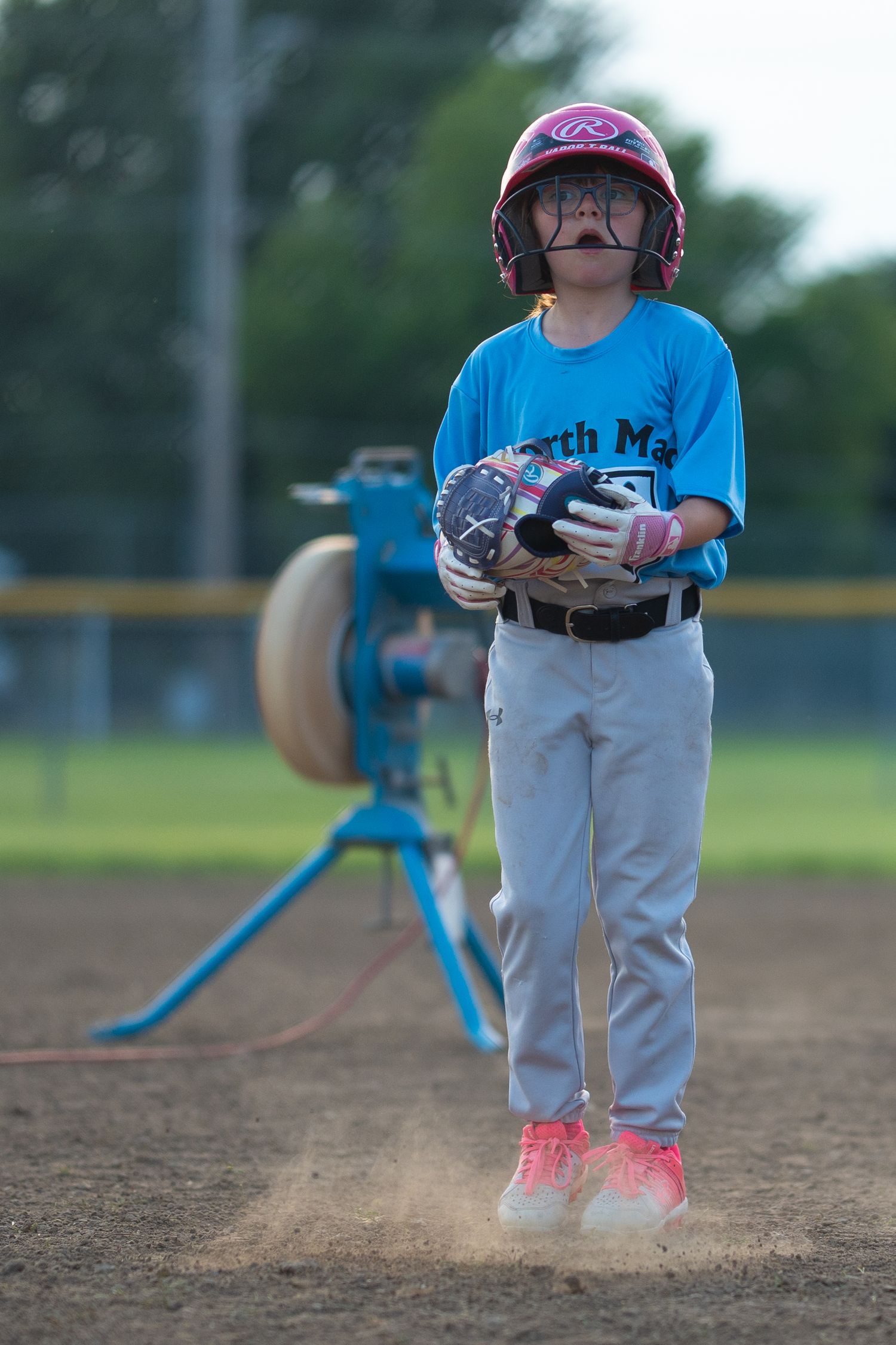 Young baseball player in uniform practicing on a dirt field at dusk.