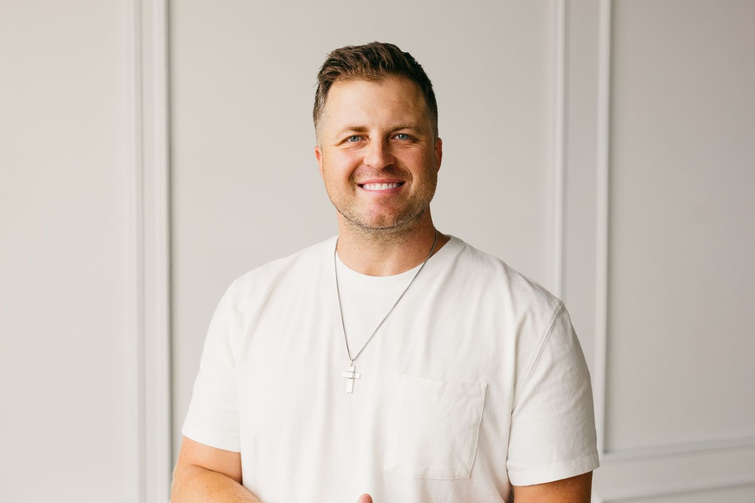 Professional headshot of someone wearing a white t-shirt smiling against a light gray background.