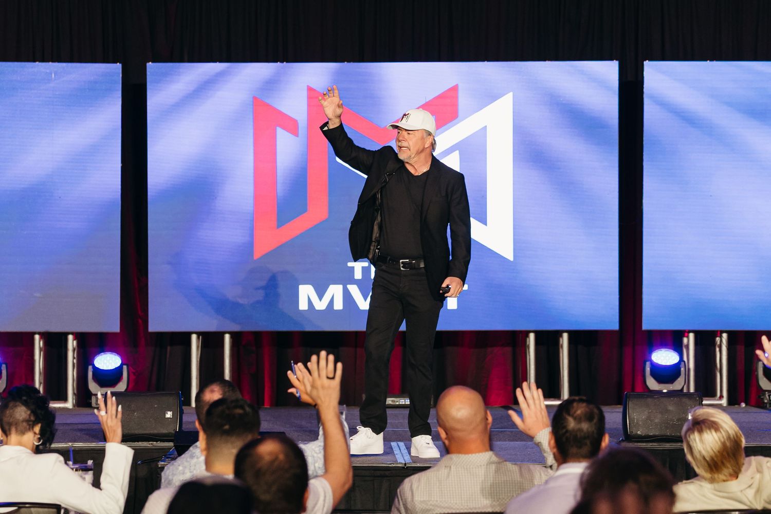 A conference presentation showing large digital displays with a presenter on stage.
