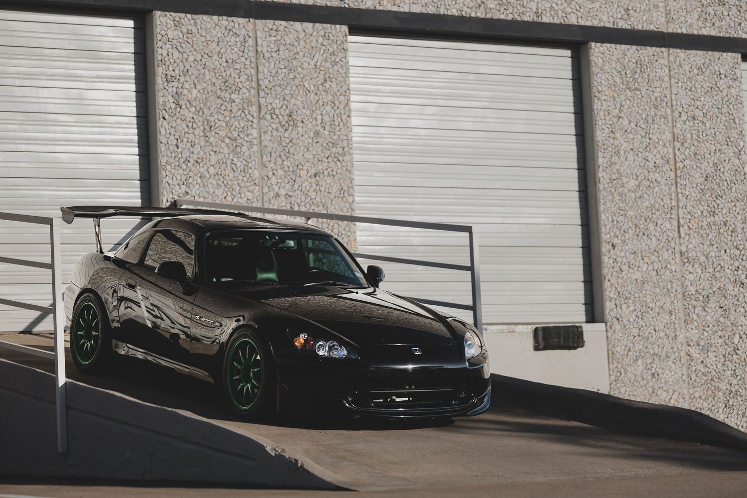 Sleek black car with custom neon green wheels parked in front of industrial garage doors.
