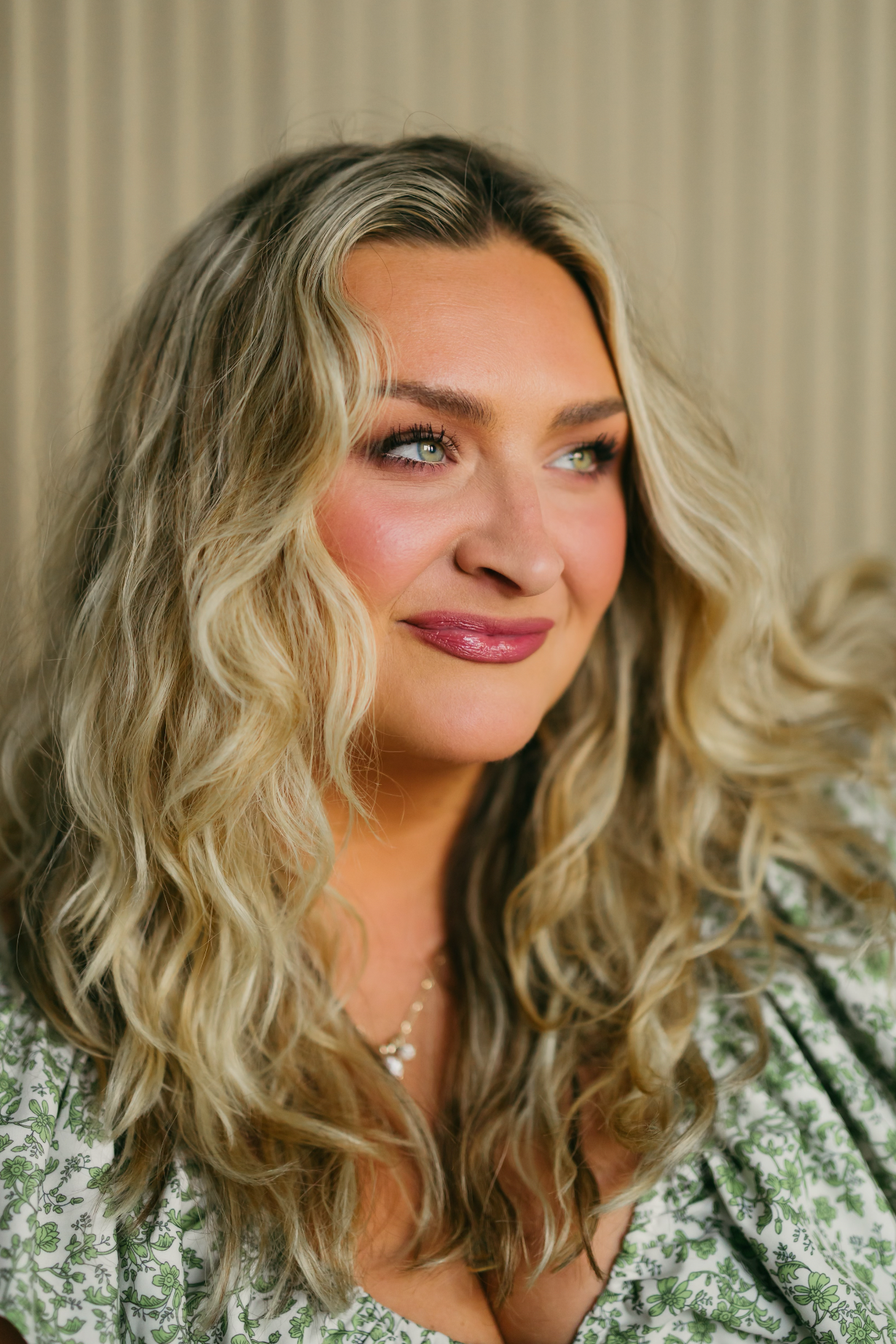 A close-up portrait shows wavy blonde hair, smokey eye makeup, and glossy pink lips against a neutral background.