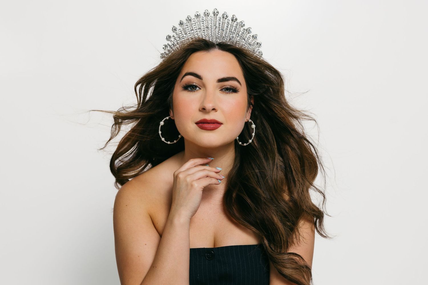 Glamorous portrait of woman in black dress and crystal crown with flowing hair.