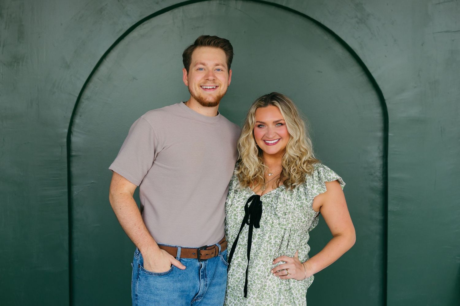 Couple posing together against green arched wall background.