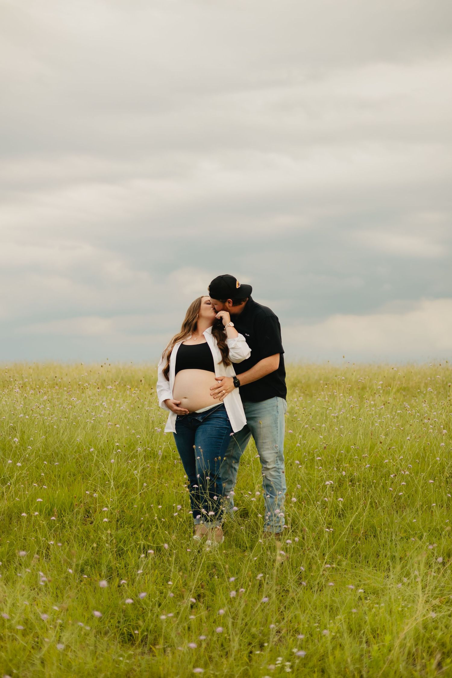 Intimate couple portraits in a serene meadow setting under cloudy skies.