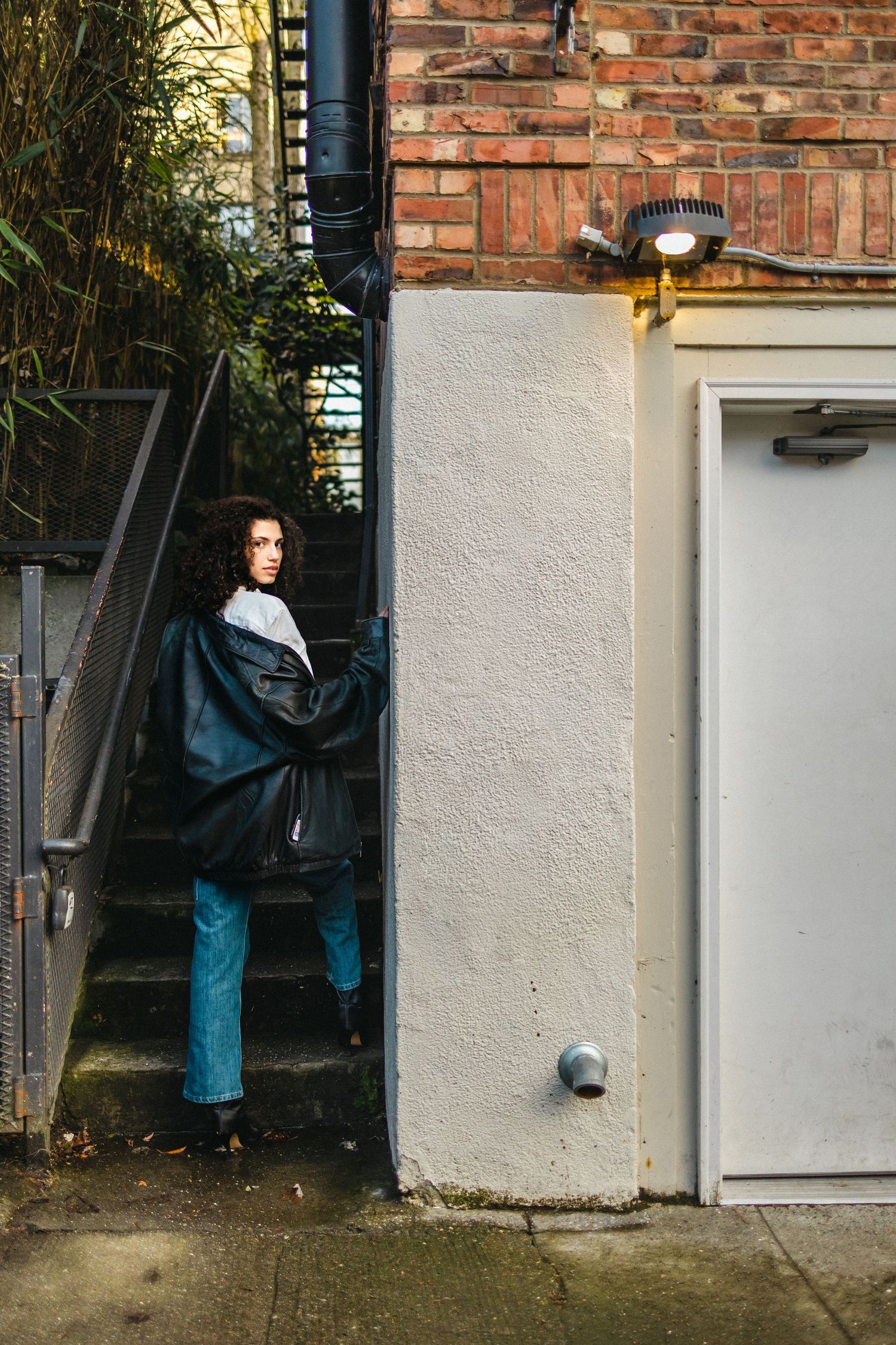 Person hanging and organizing dark clothing on a white outdoor wall against red brick background.