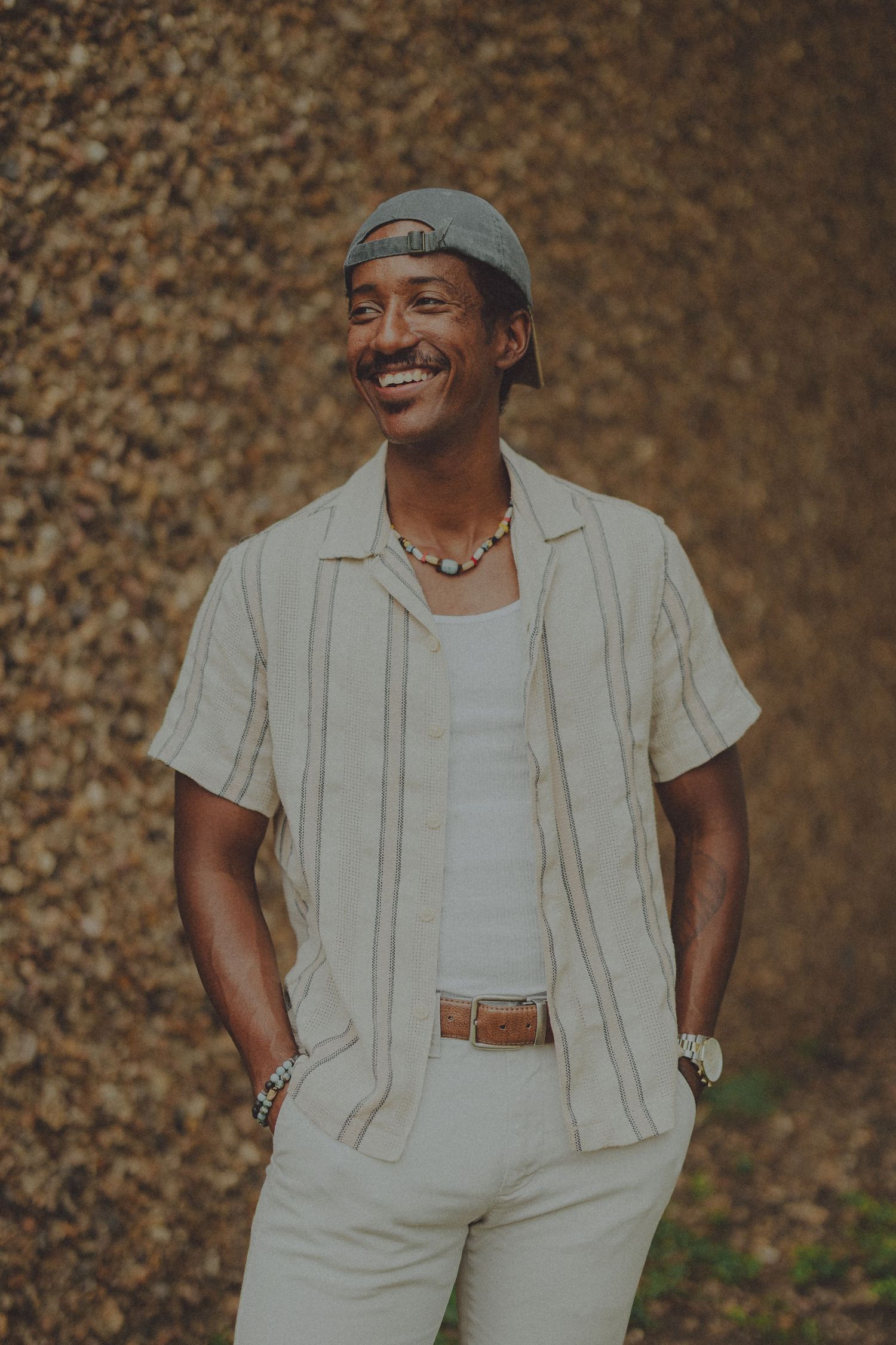 A series of fashion portraits showing someone wearing a casual beige linen outfit with a white undershirt and cap against a textured wall.