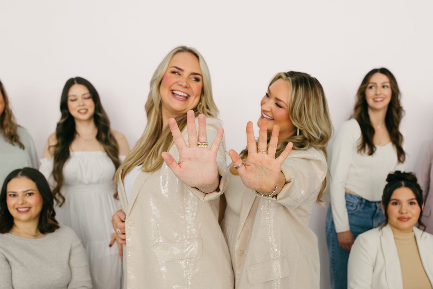 Joyful women in light-colored outfits laugh together during a group photo session.