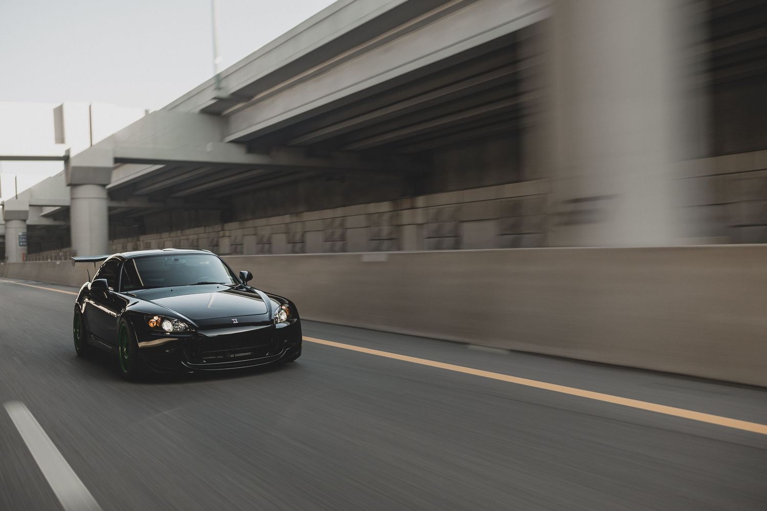 Black sports car speeding under highway overpass on urban road, motion blur background.