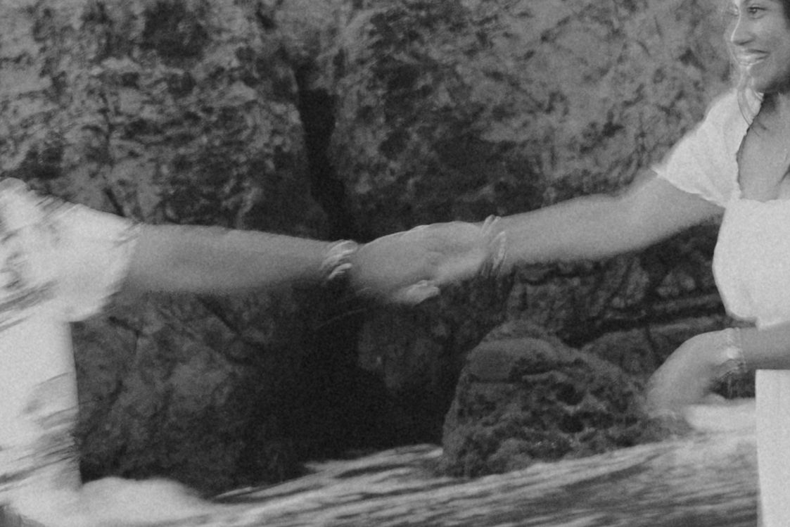 Two people shaking hands outdoors near rocky cliffs in a vintage black and white photograph.
