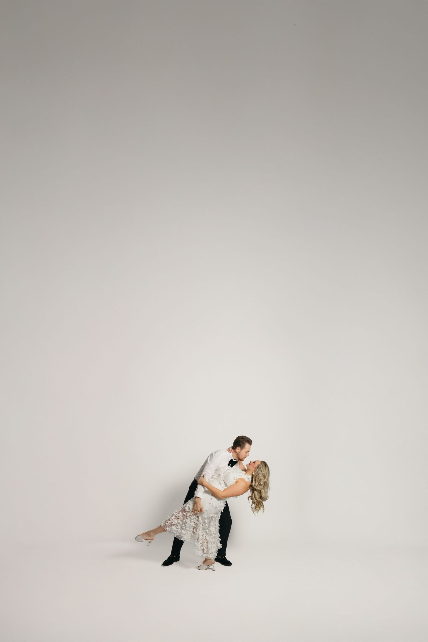 A couple shares a romantic dip kiss while dancing against a clean white studio background.