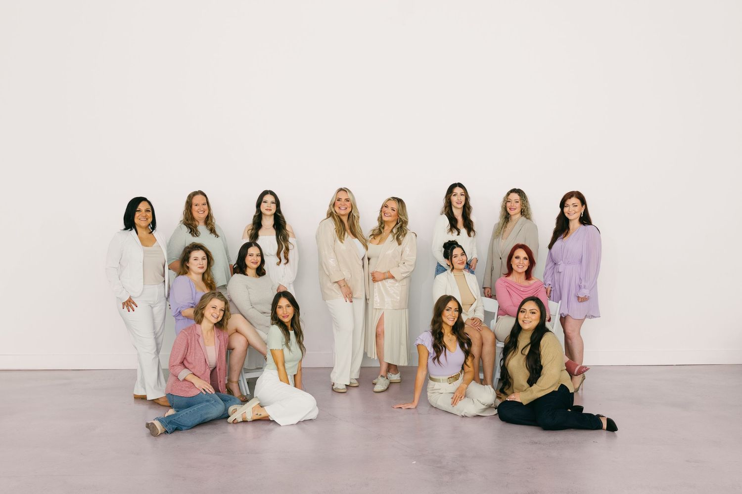 Group of women posing together in pastel outfits against a white wall for a professional photo shoot.