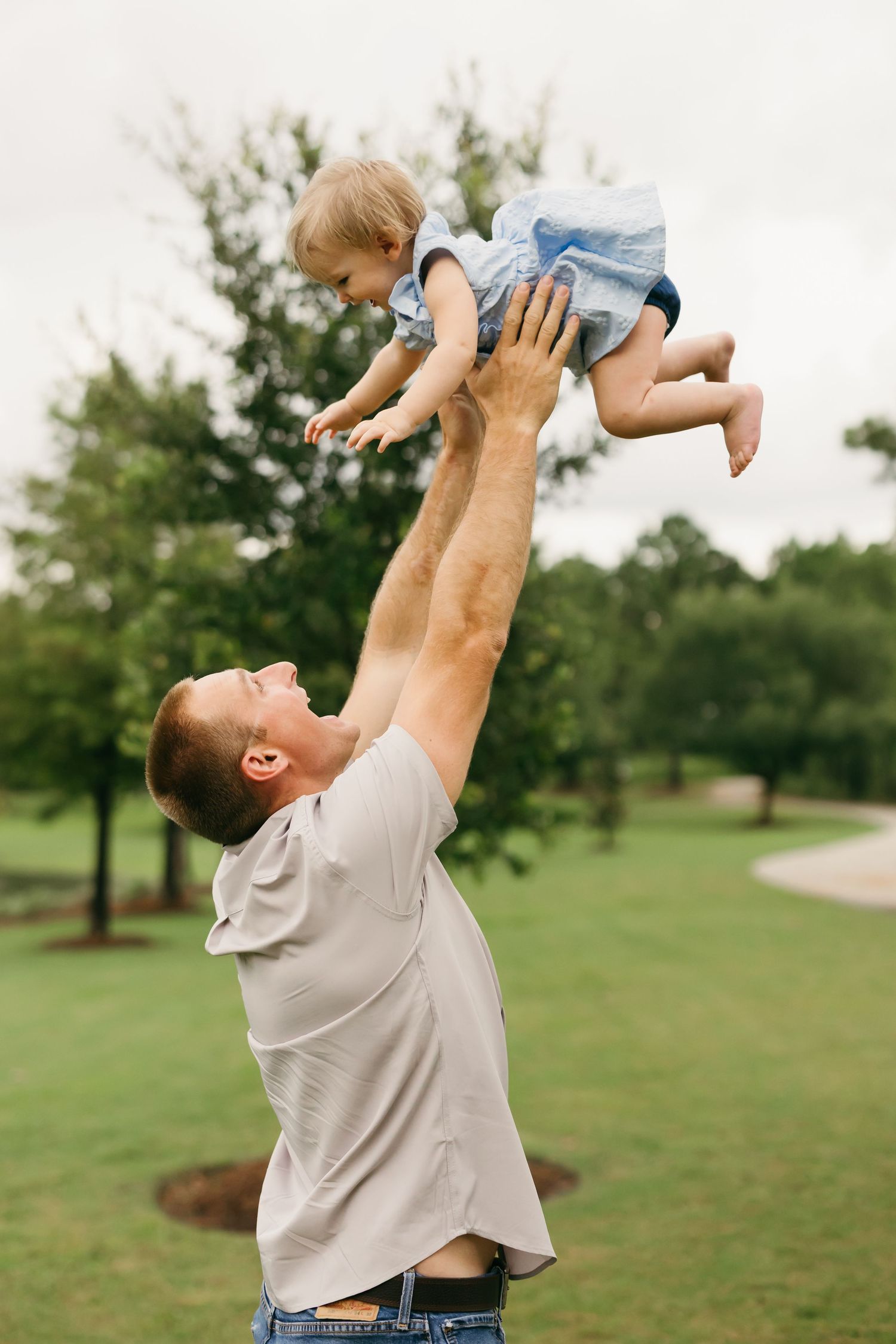 Parent lifting and playing with small child in blue outfit on grassy field.
