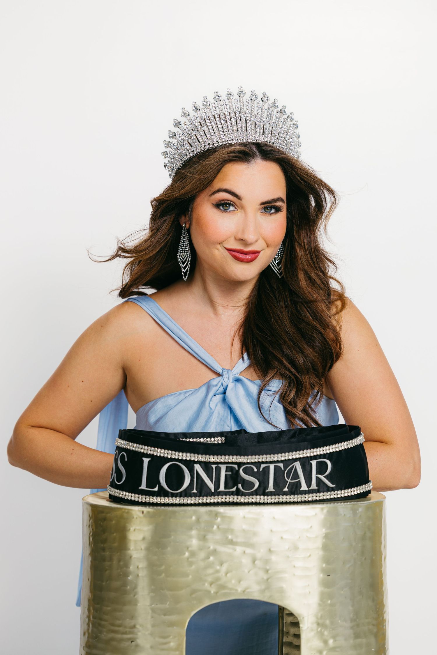 Beauty pageant contestant wearing crown and sash poses in blue dress.