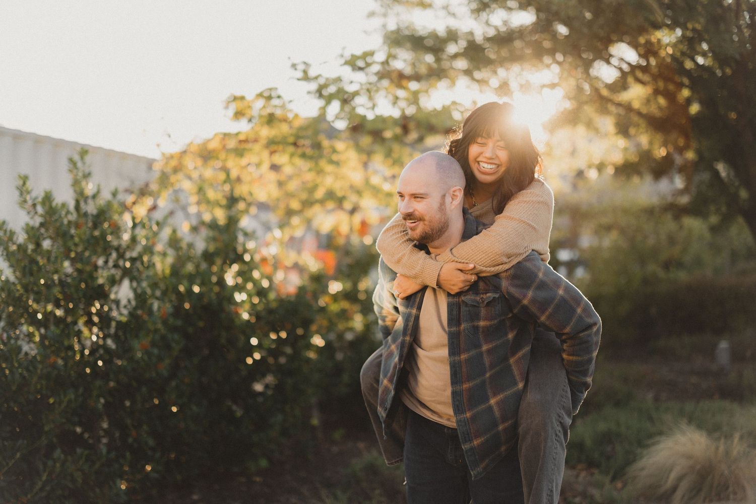 Couple embracing outdoors during golden hour with sun flare in background.