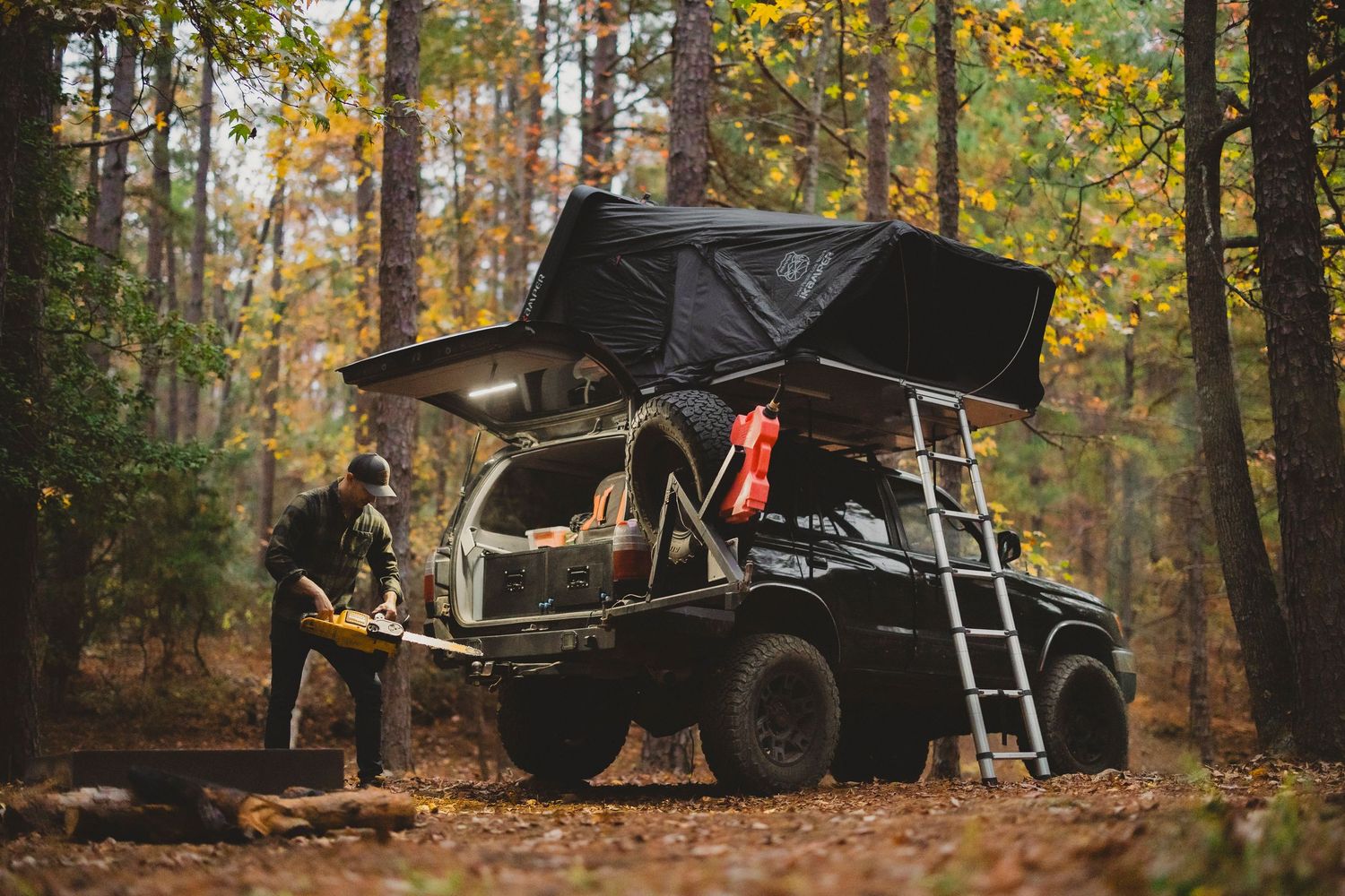 Row of off-road vehicles and camping equipment in autumn forest setting.