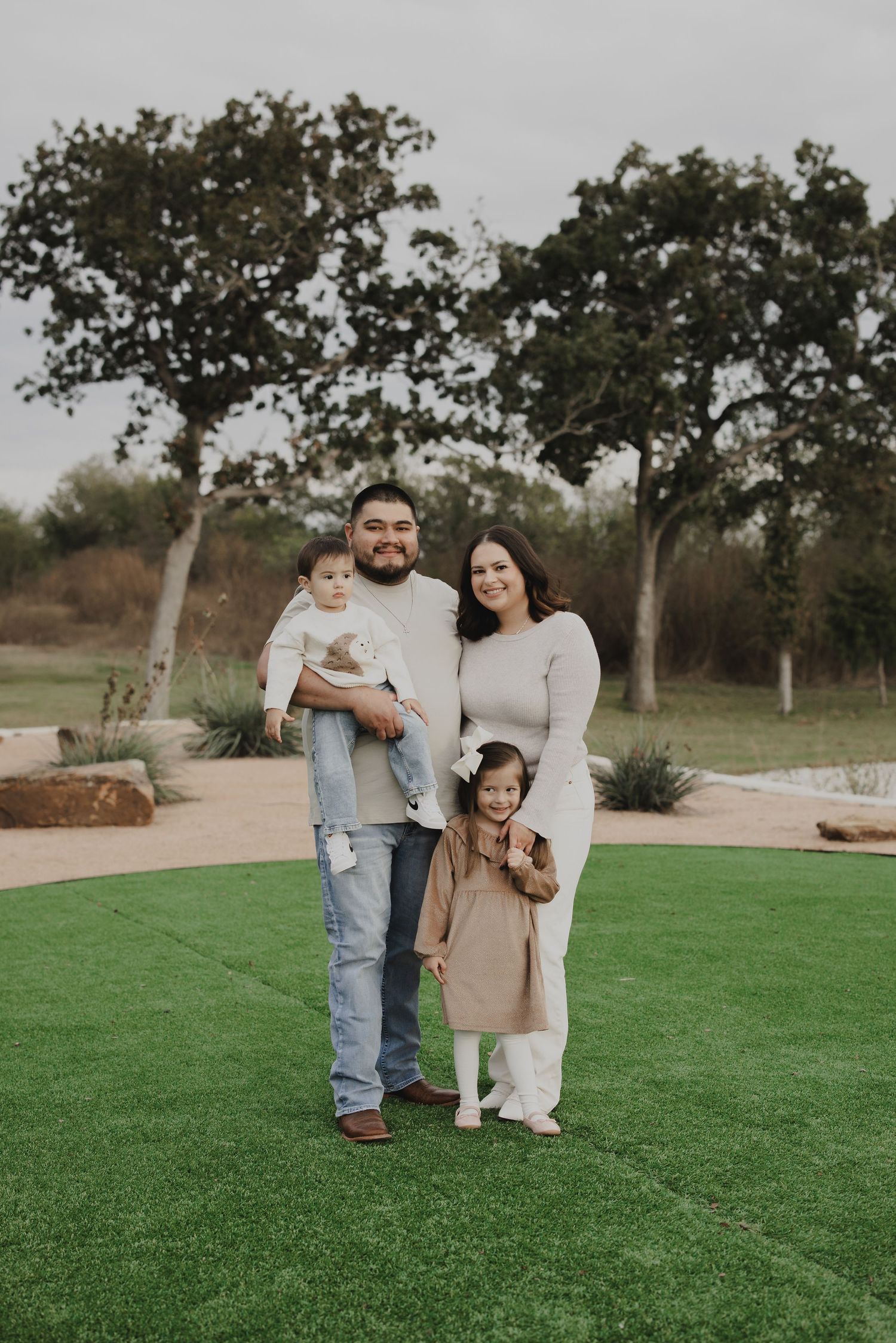 Family posing together on well-maintained green lawn with trees in background.