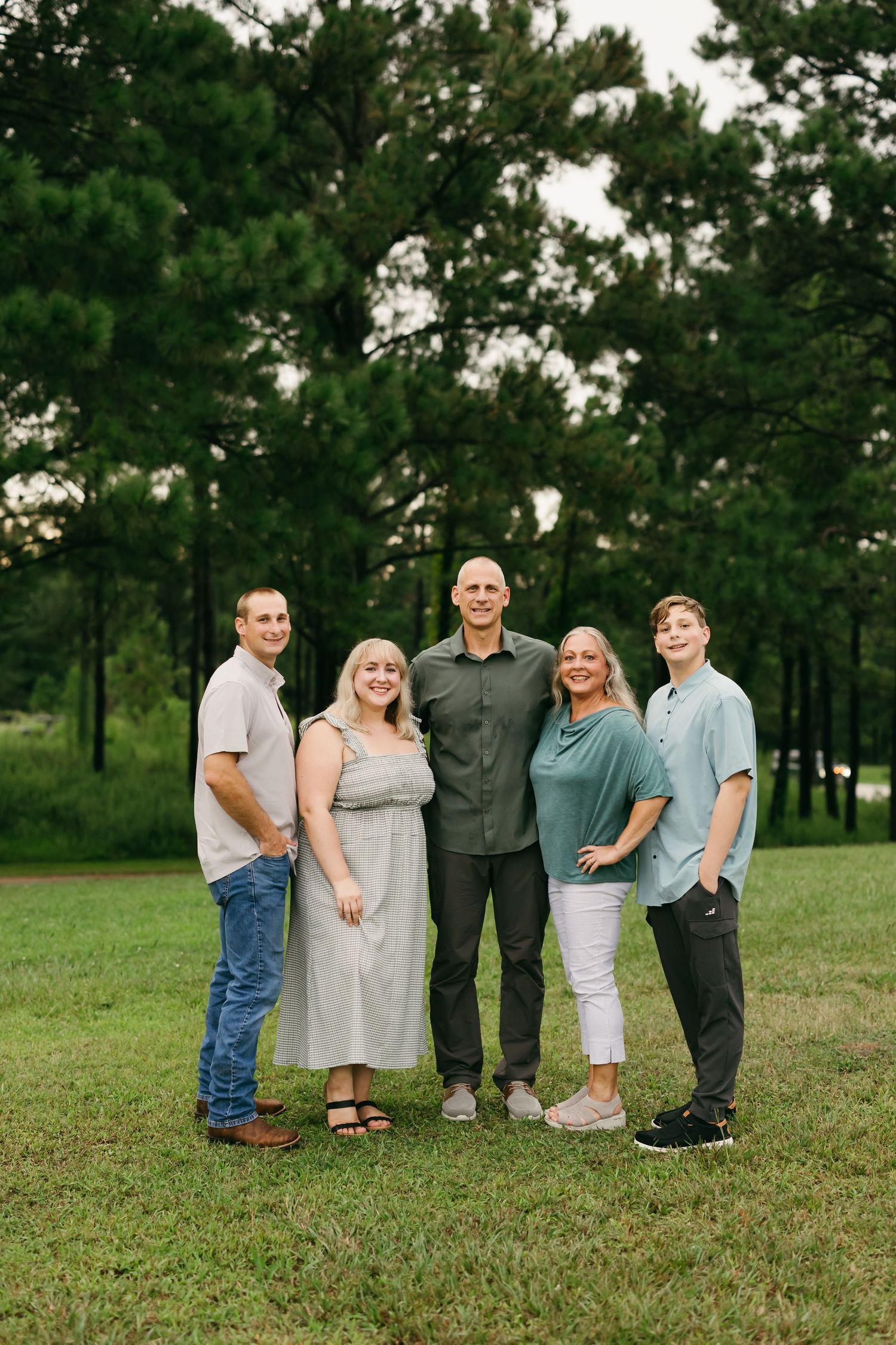 Group photo session of family members sitting together on grassy field at sunset.