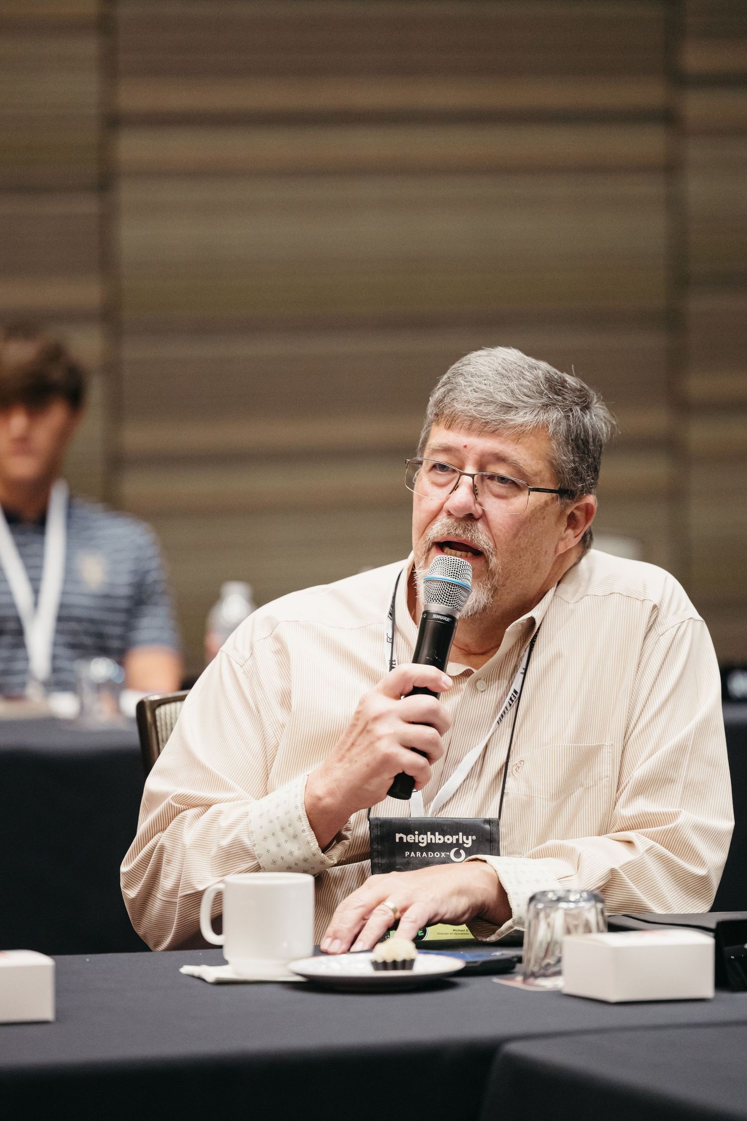 Enthusiastic panelist in baseball cap speaks at conference table during discussion.